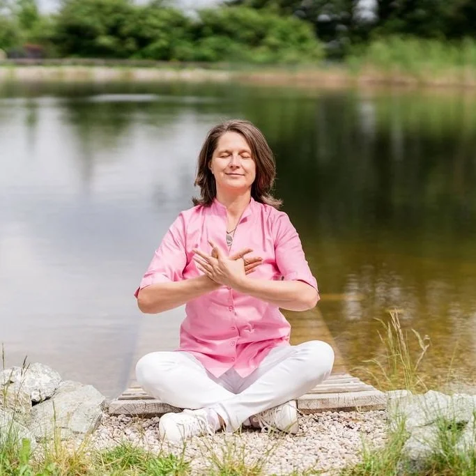 Elke Pfaffeneder sitzt in Meditation am See und verbindet sich mit Ruhe, innerer Balance und Herzlichkeit.