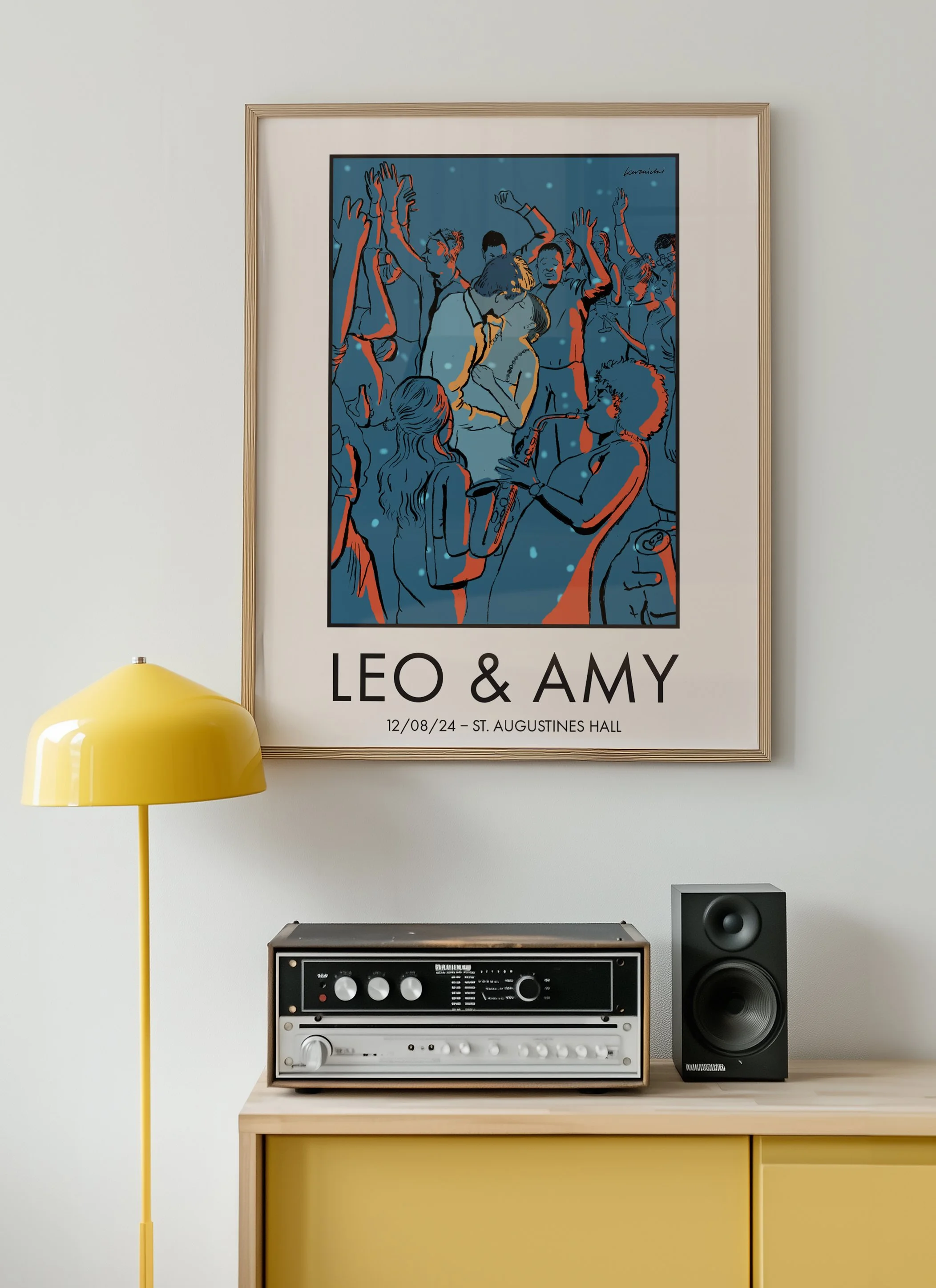 A framed poster on a white wall features an illustration of people dancing at a party, with the names Leo & Amy and the date 12/08/24 at St. Augustines Hall. Below the poster, a yellow floor lamp stands next to a vintage stereo system and a black spe