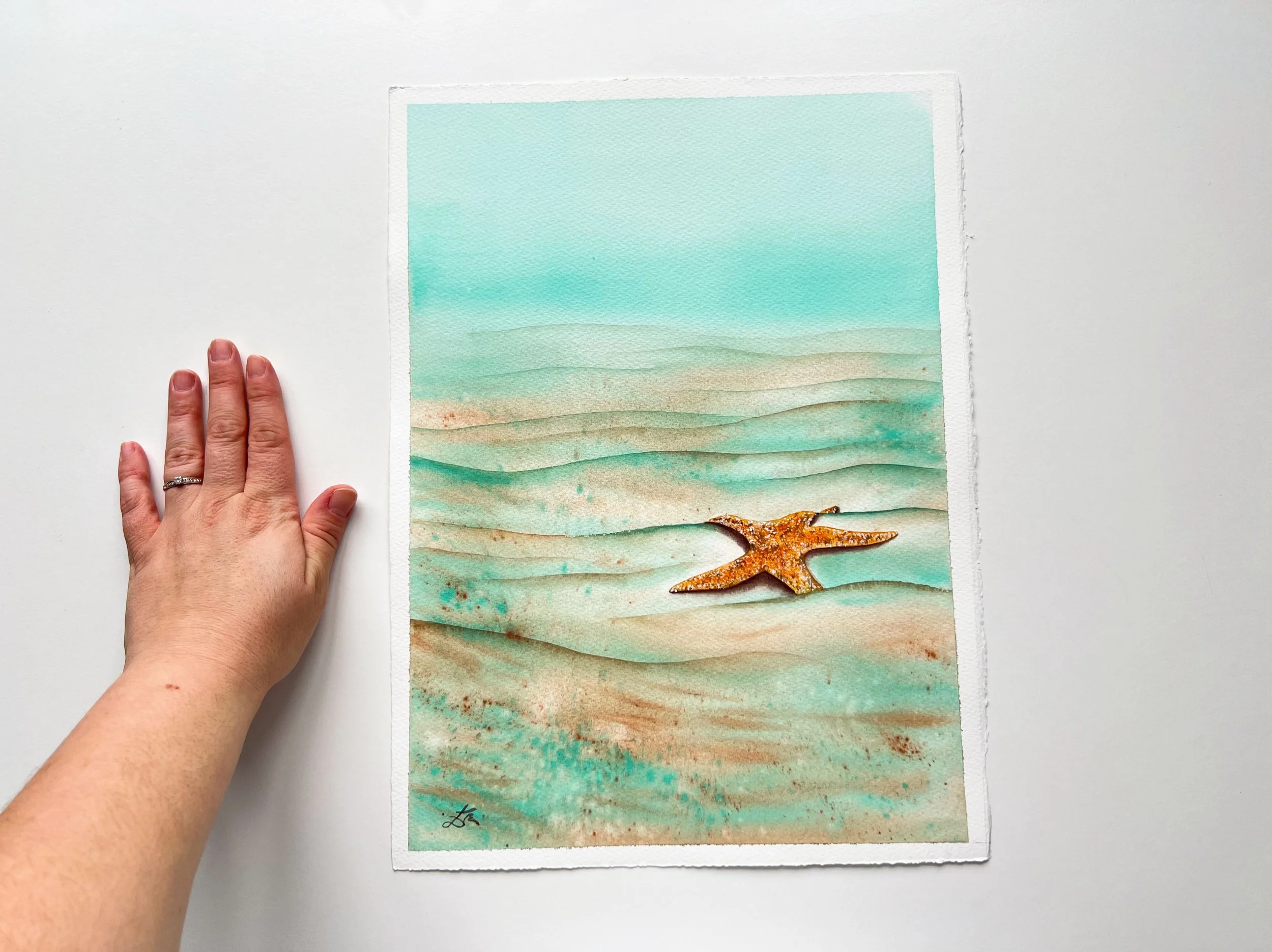 Close up from Starfish Watercolor Painting next to my hand. This is underwater Marine life art for kids or adults who love vibrant art.
