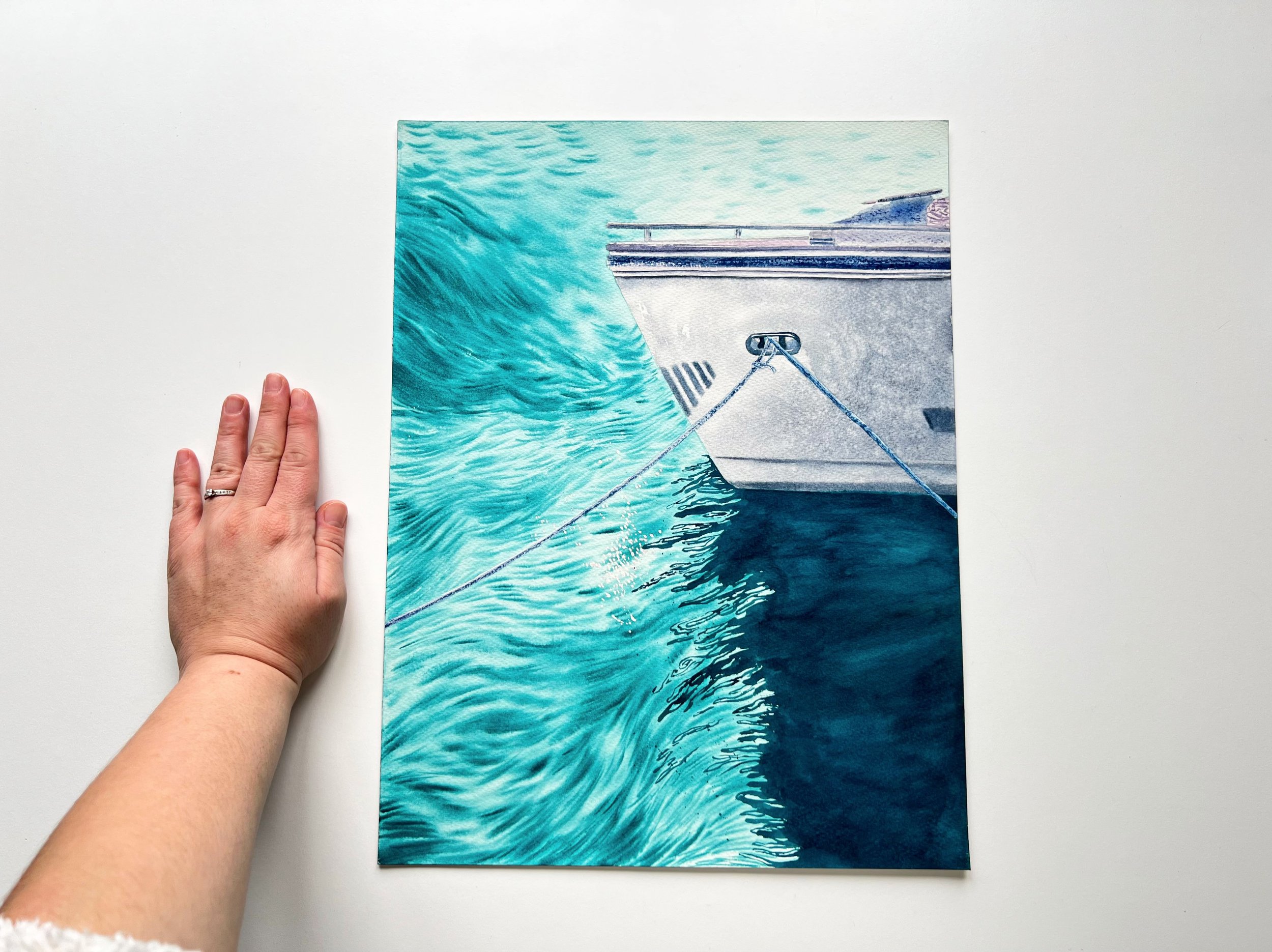 Closeup with my hand of the original watercolor painting "Wind" showcasing a majestic boat with choppy water, rope details, and shimmering reflections.