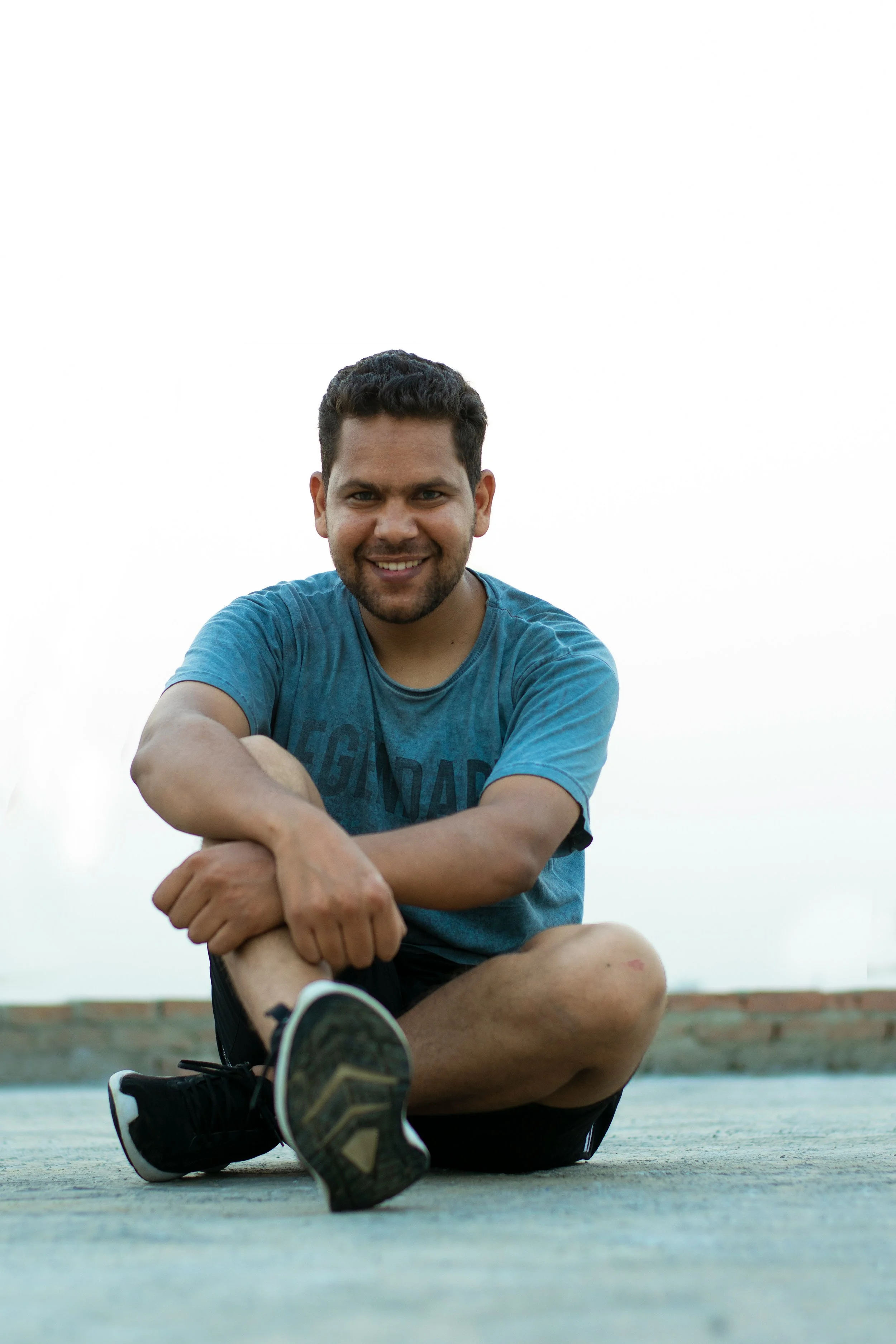 south asian man in sports kit sitting on ground and smiling