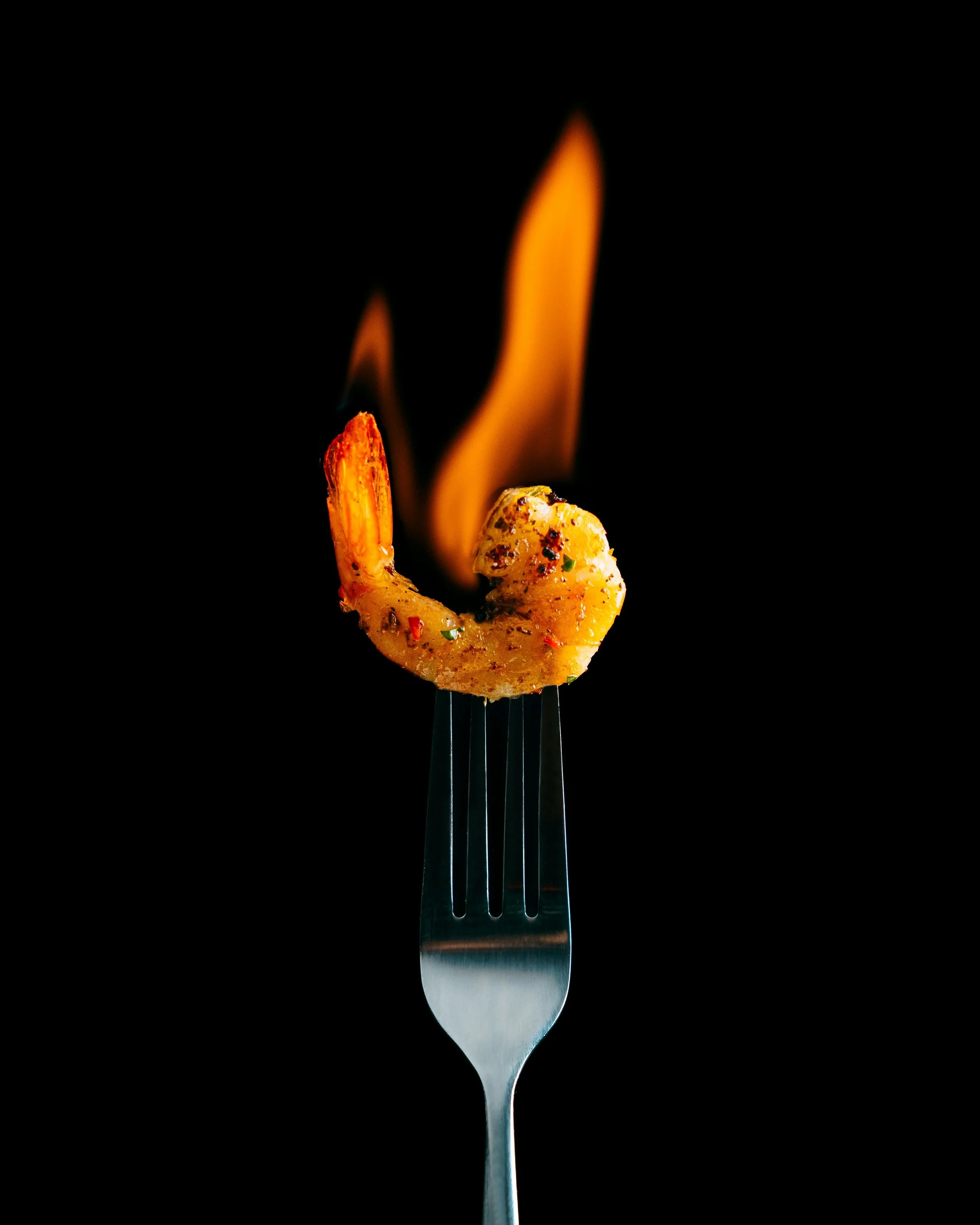 photo of a cooked prawn aflame on the prongs of a fork