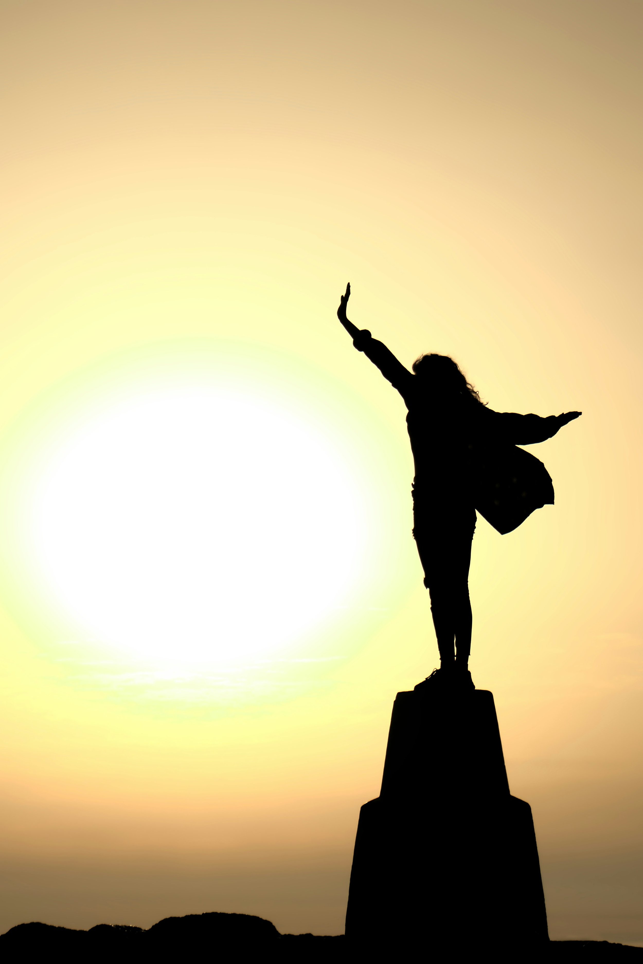 photo of a female silhouette in a cape with arms outstretched against a setting sun