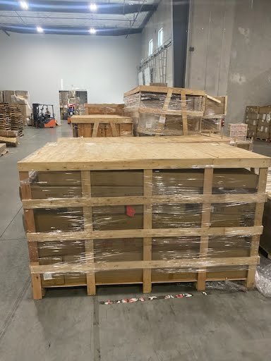 Large wooden crates stacked on a concrete warehouse floor with additional crates and pallets in the background.