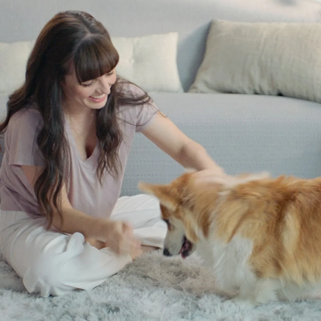 Women with long brown wavy hair playing with her Corgi dog