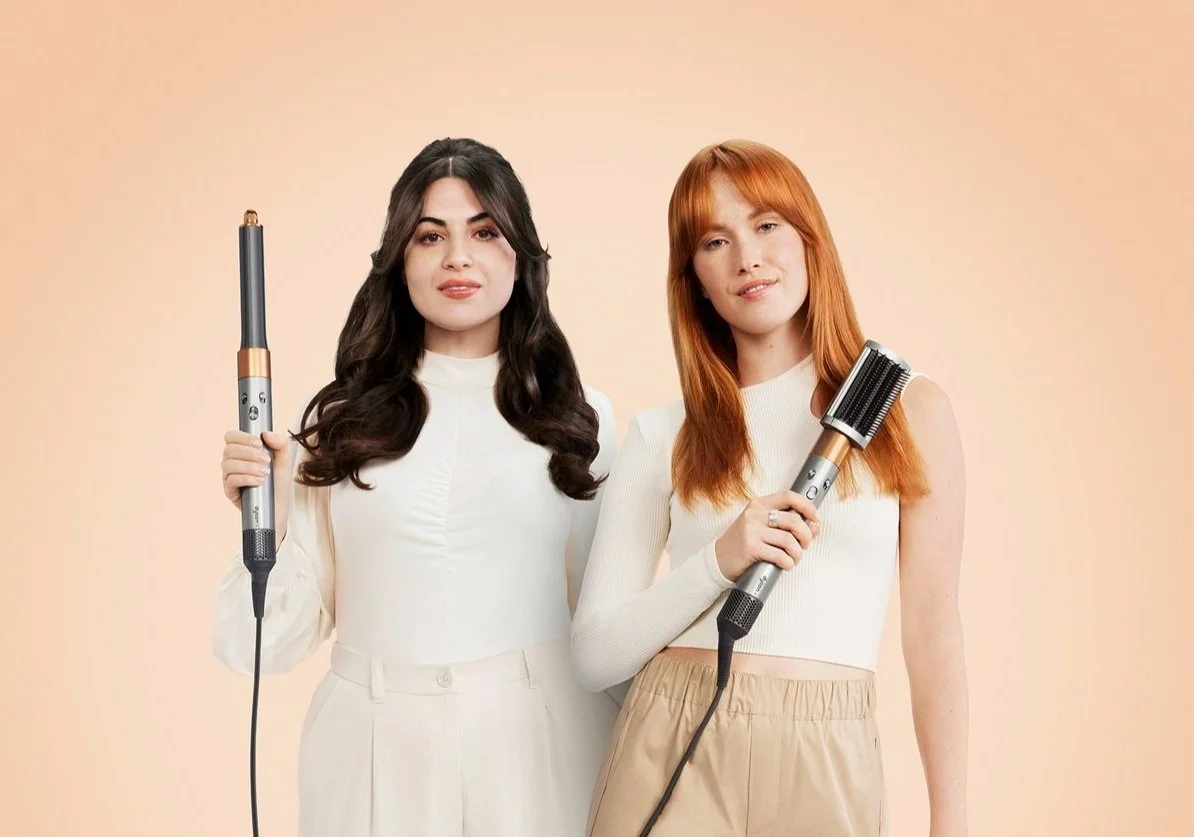 Two women posing holding the Dyson Airwrap