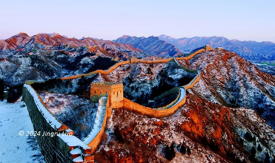 The Great Wall of China winds along a ridge through a snow-covered mountainous landscape on a cold winter day.