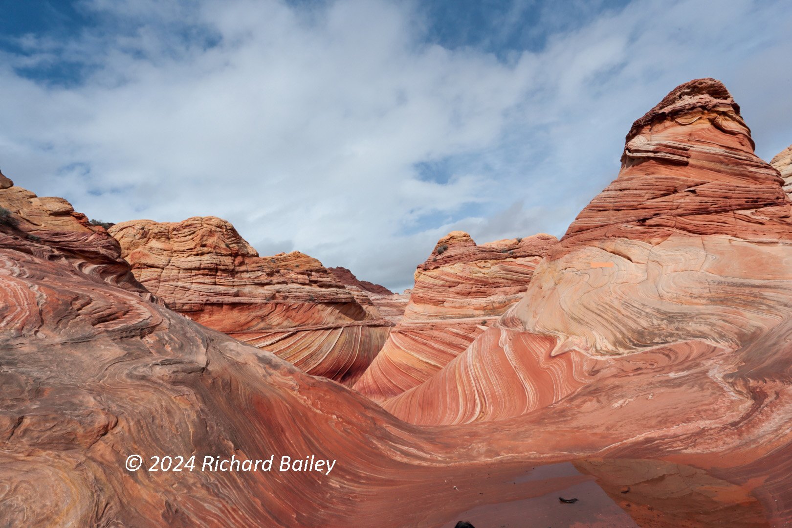The swirling sandstone formation known as The Wave in northern Arizona, its banded rock curving under a clear blue sky.