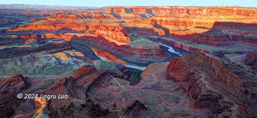 A panoramic view of the canyon at Dead Horse Point State Park, Utah, with the Colorado River winding through rugged red cliffs in sunset light.