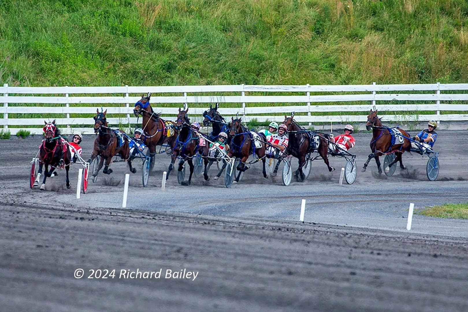 Harness racing horses and drivers in sulkies round the turn on a dirt track at Monticello Raceway, New York.