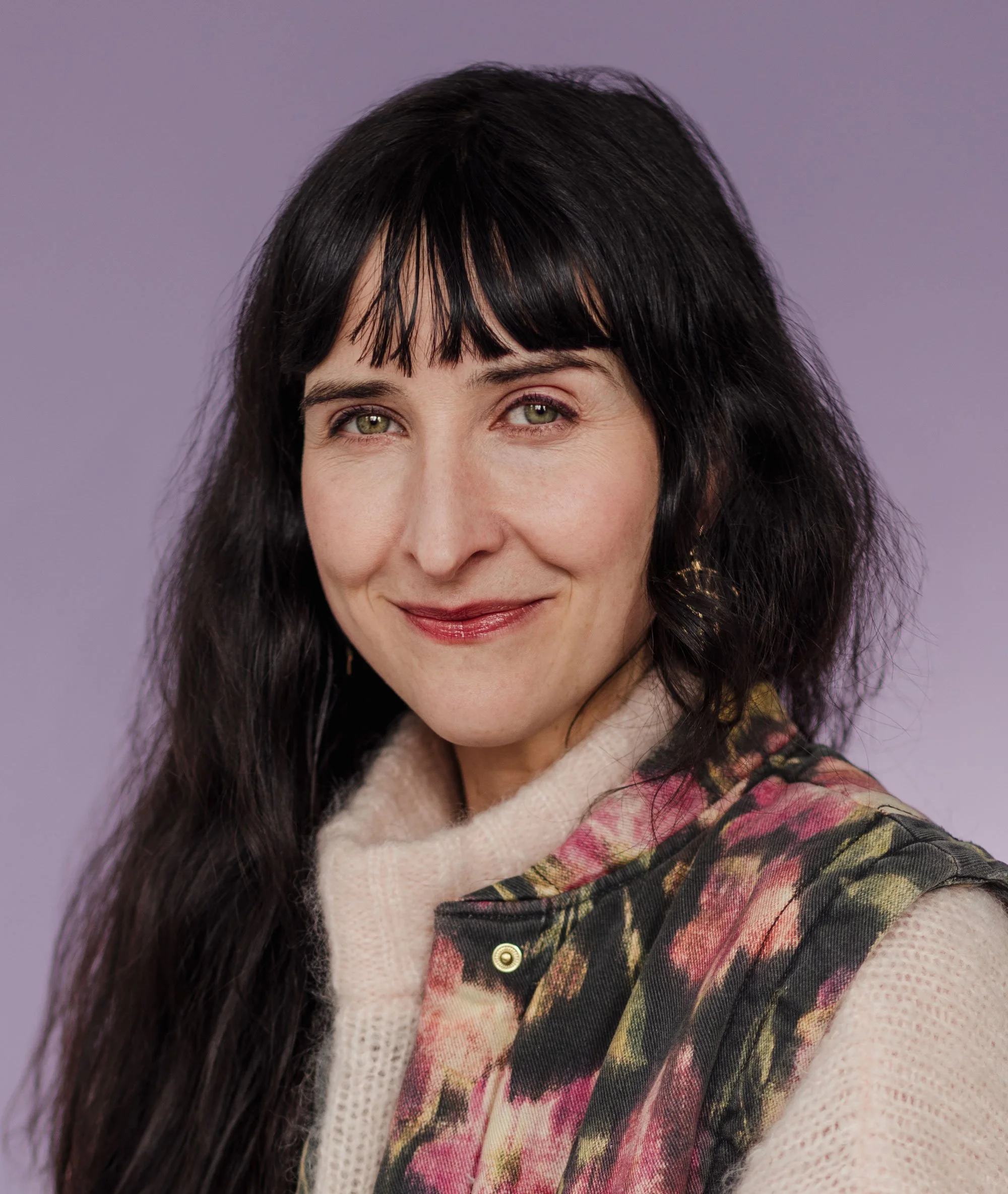 Portrait d'une femme avec des cheveux noirs, un vêtement à motifs floraux et un fond violet.