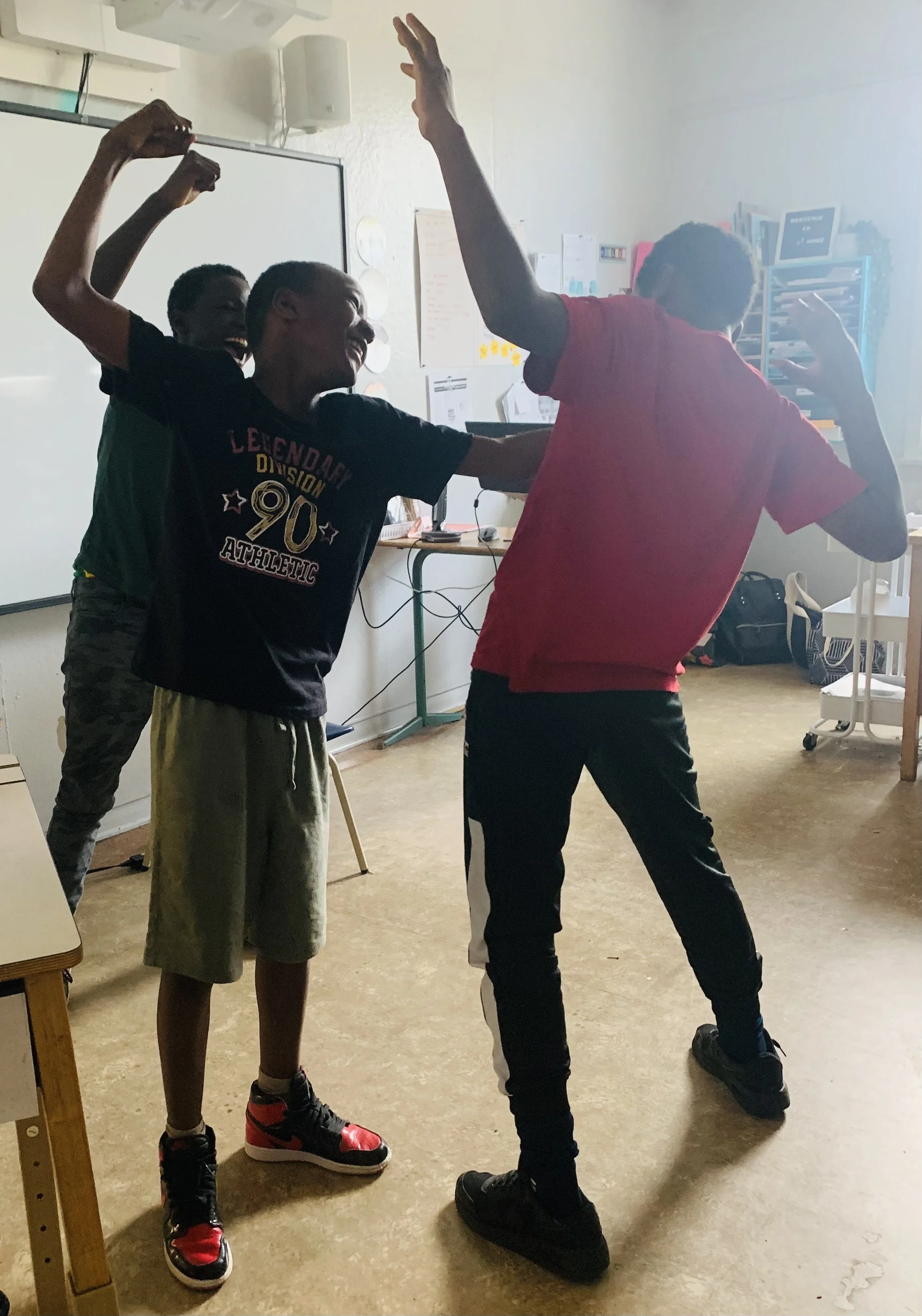 Trois enfants semblent jouer ou faire une activité amusante en classe, avec des expressions joyeuses et des gestes dynamiques.