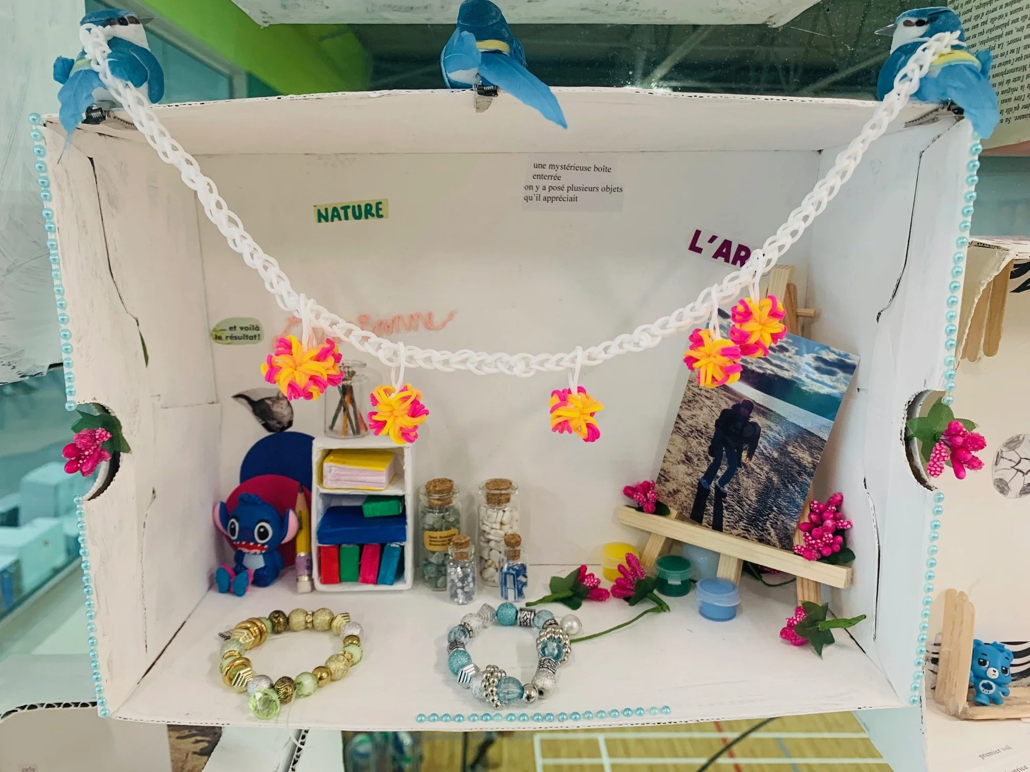Une petite boîte créative avec des décorations en figurines, photos, bijoux, et éléments naturels, portant des inscriptions en français.