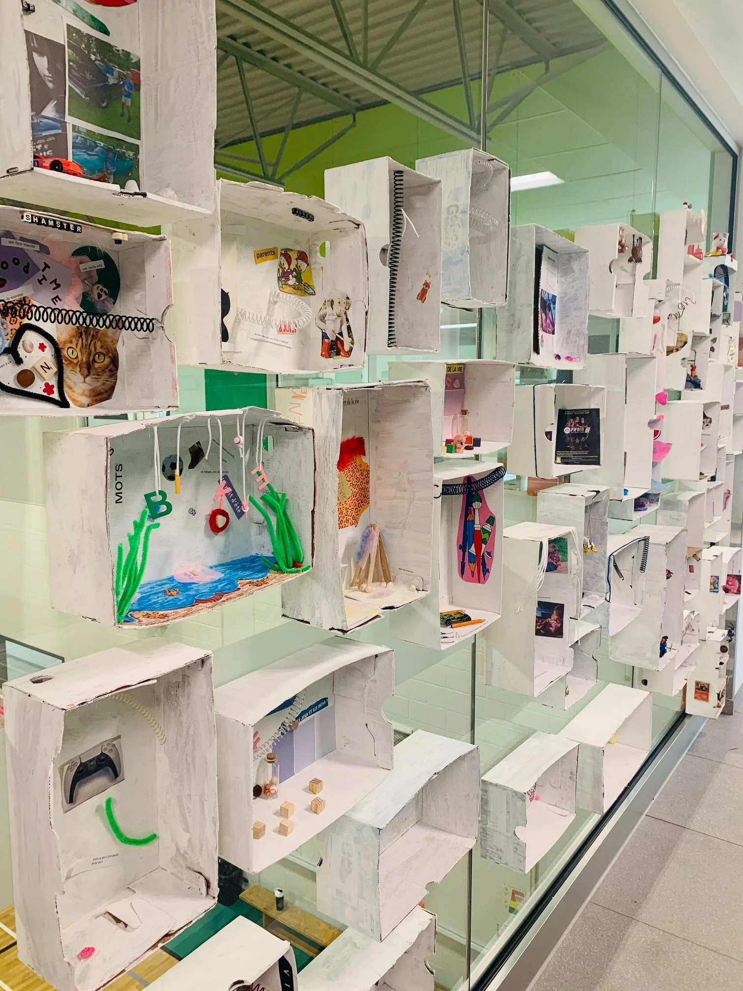Une vitrine contenant de nombreuses petites créations artisanales dans des boîtes en bois peintes en blanc, exposées sur plusieurs rangées.