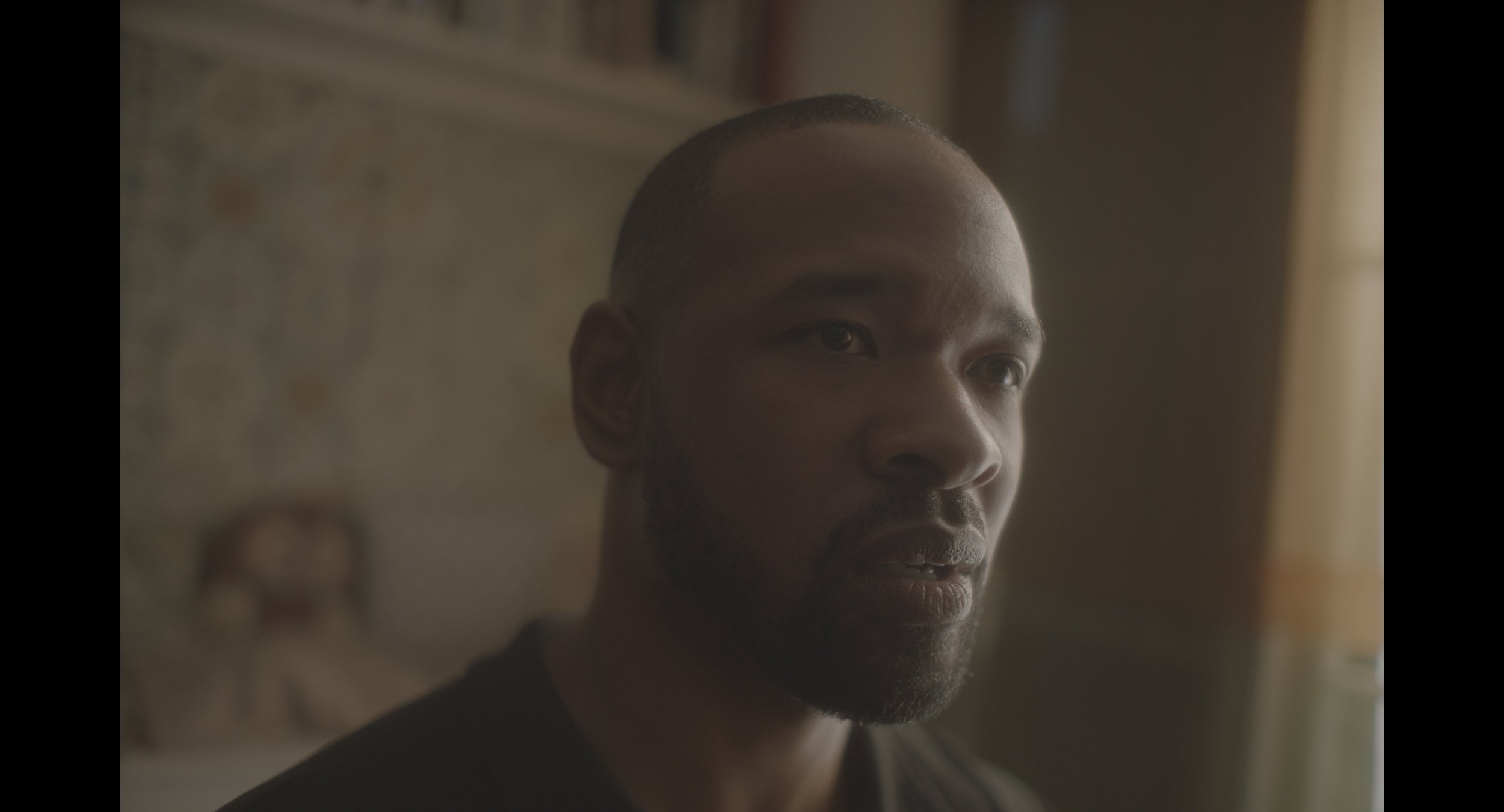 Close-up of a thoughtful man indoors, softly lit background.