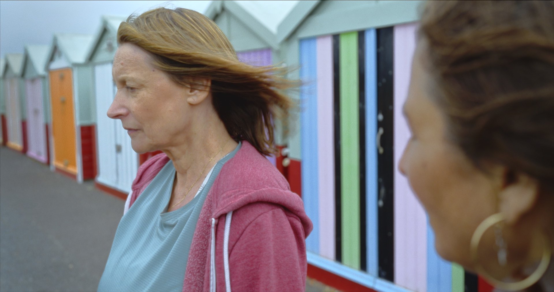 Two women walking along a row of colorful beach huts.
