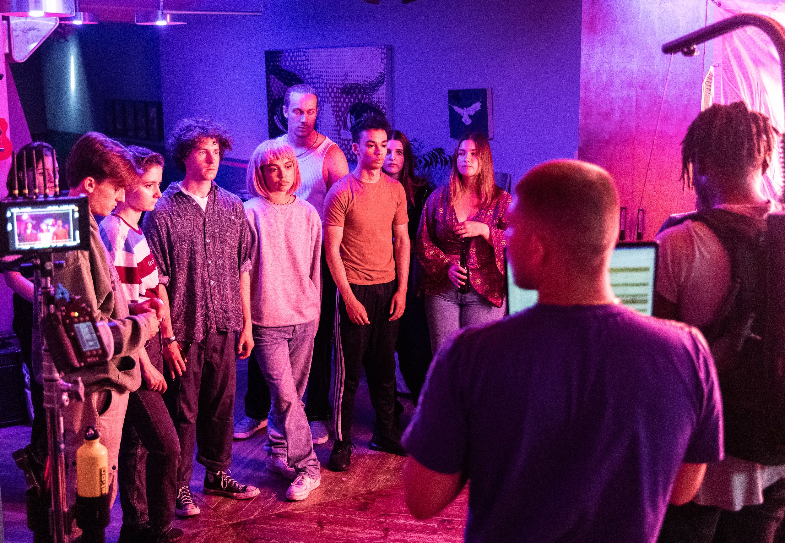 Group of people on a film set with vibrant lighting, including cameras and crew members.