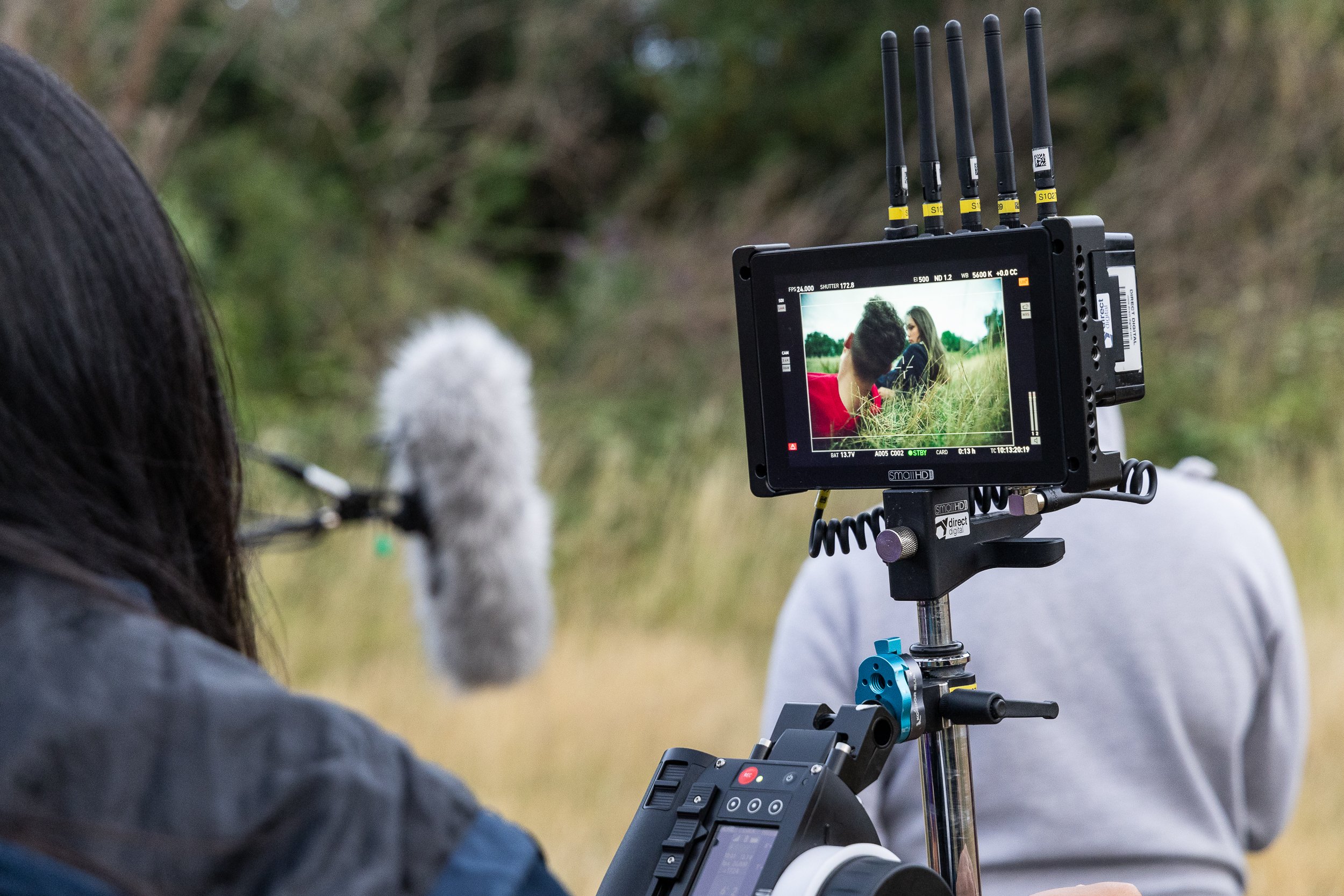 Filmmaker monitoring a scene on a screen during an outdoor shoot, with a microphone and crew member visible.