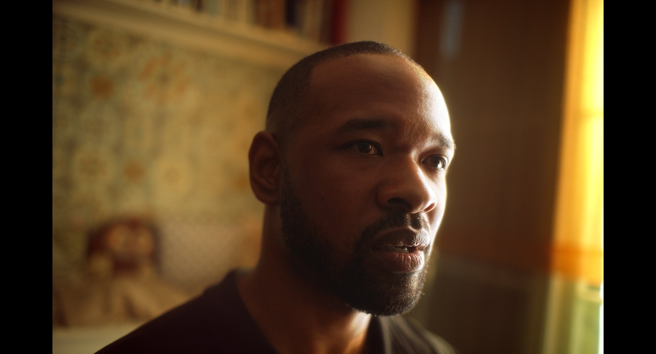 Close-up of a man with a beard looking thoughtfully in a room with blurred background.