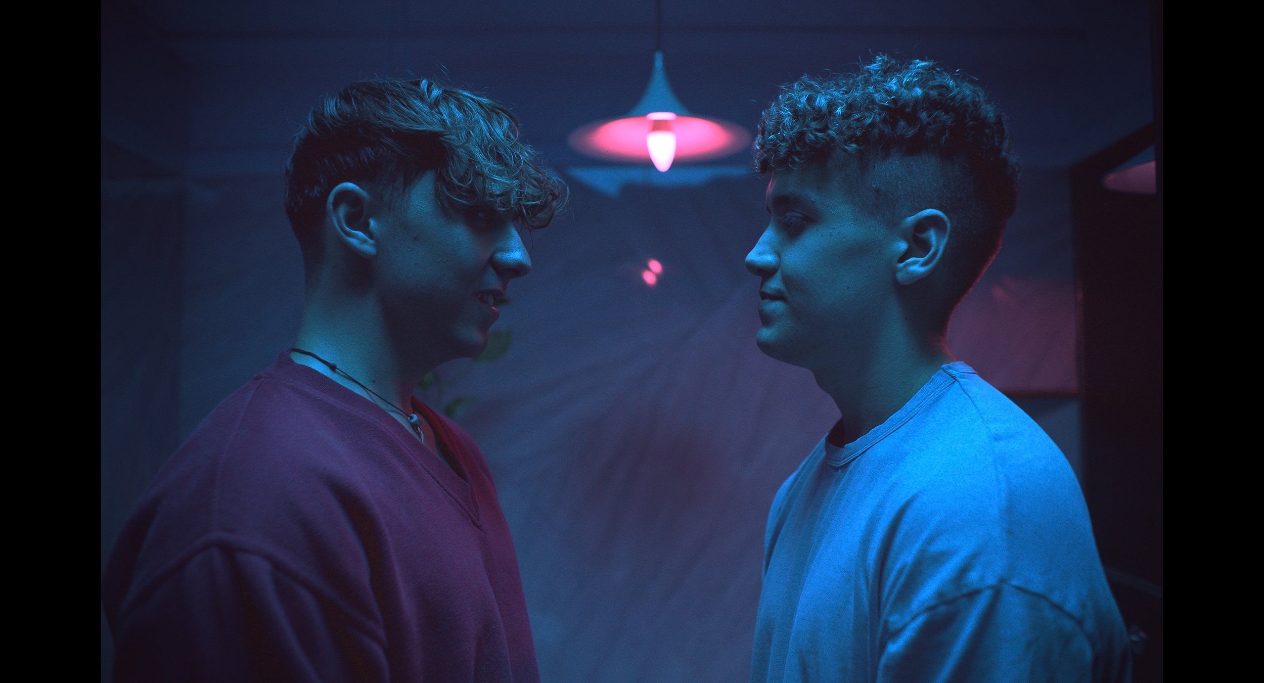 Two people facing each other in a dimly lit room with blue and pink lighting.
