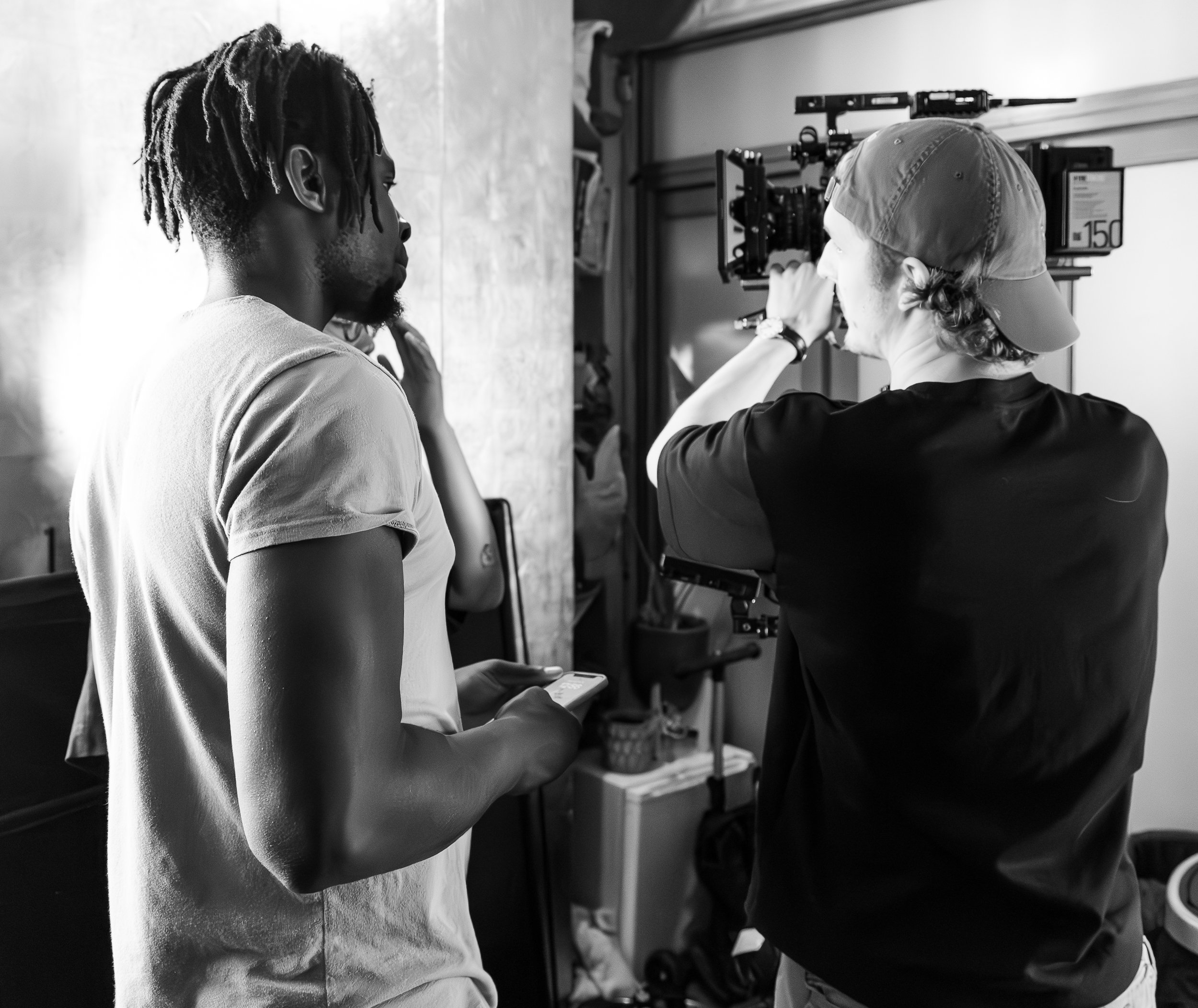 Two people on a film set; one holds a camera while the other looks on with a phone.