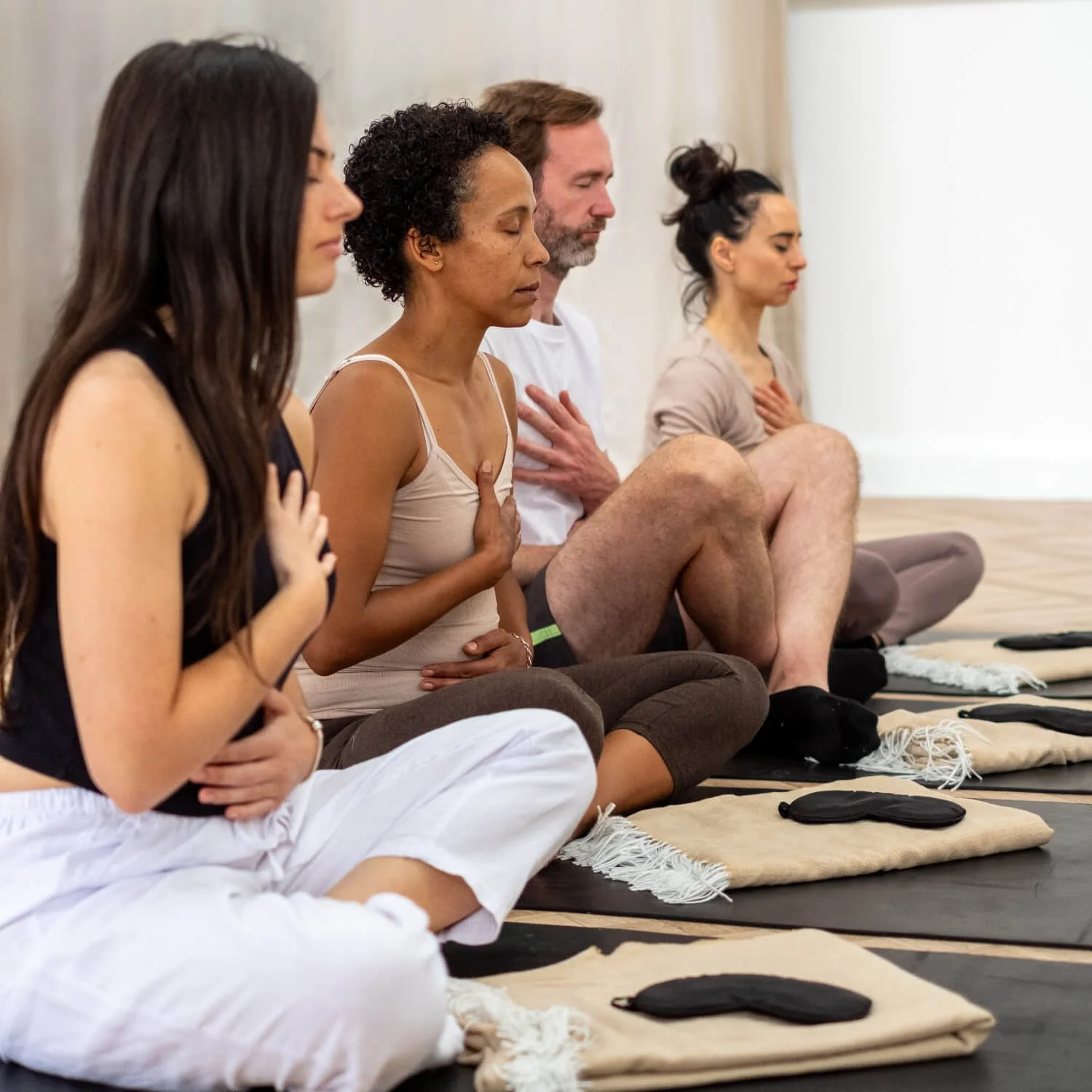 A diverse group of people sitting on Yoga mats, practicing meditation with hands on their chests and eyes closed.