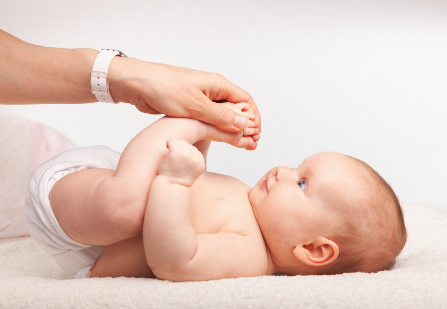 Ein Baby bekommt die Beine, als Teil einer osteopathischen Behandlung, durchbewegt.
