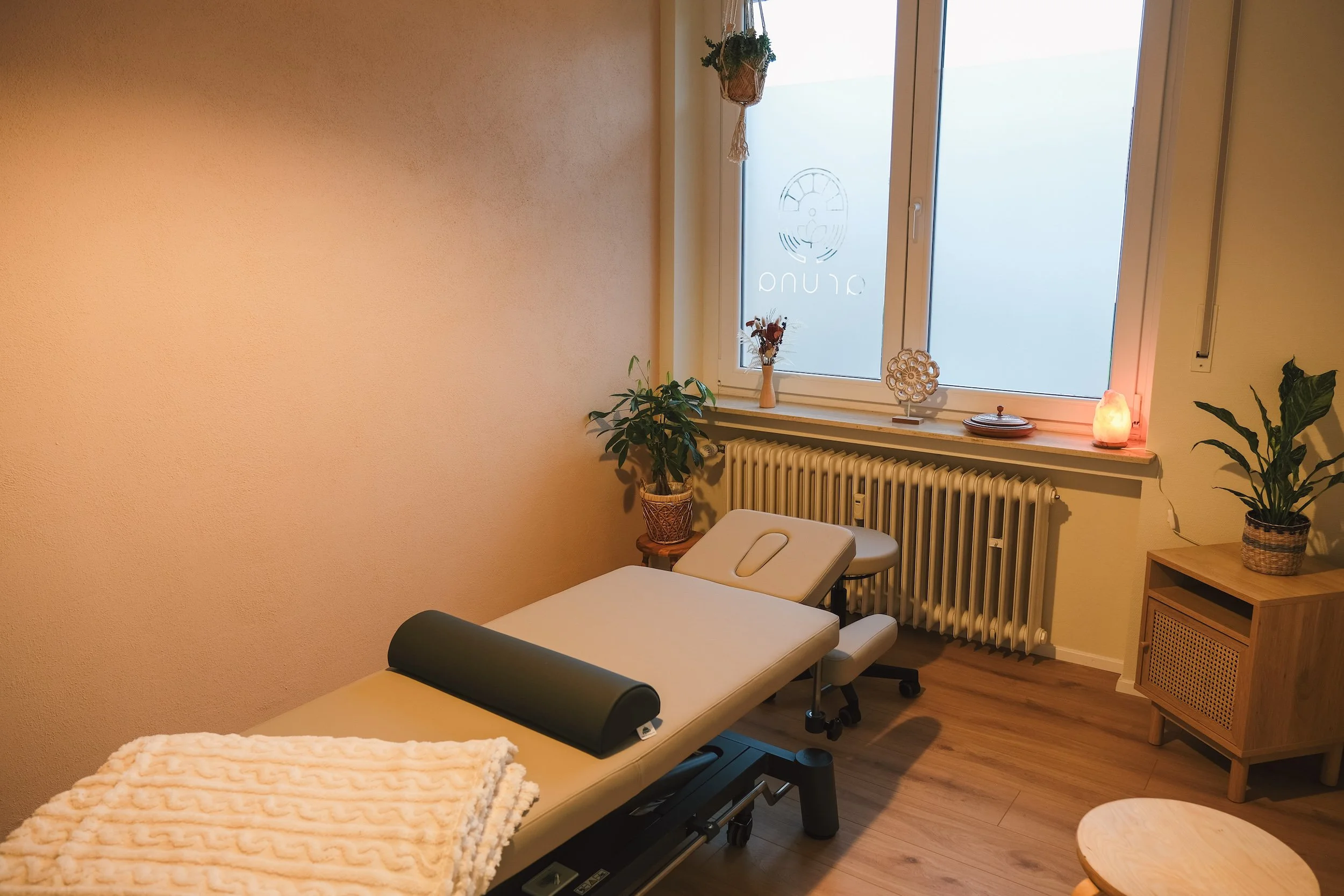Ein Behandlungsraum für Osteopathie und Kinésithérapie mit einer Behandlungsbank, Grünpflanzen und Deko.