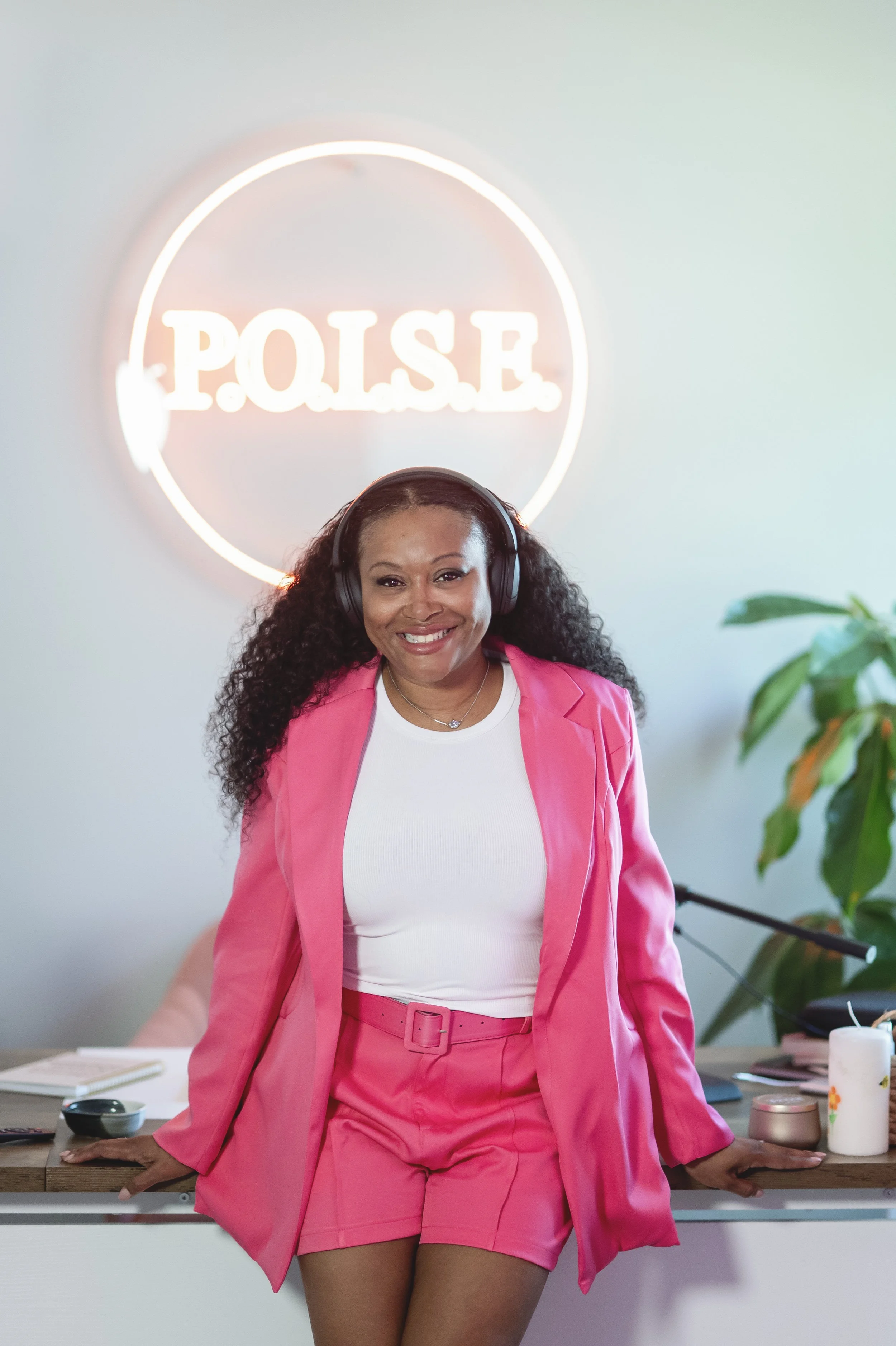 Charise Beckett, host of Queens Behind the Scenes, wearing a pink suit in the P.O.I.S.E. studio