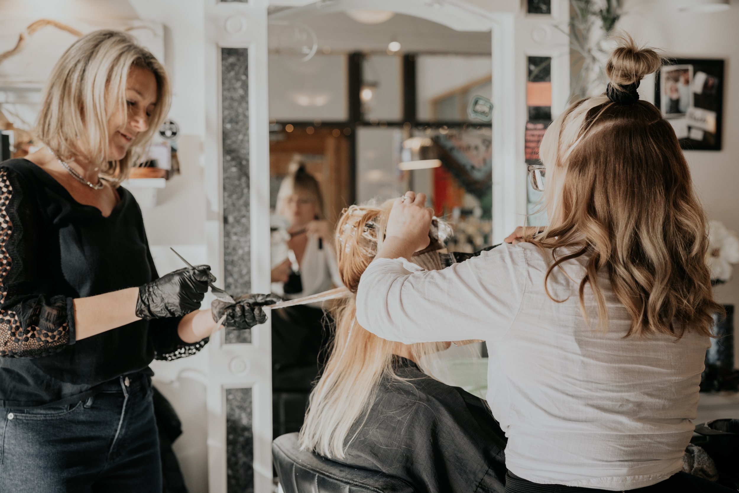Two stylists coloring a blond client's hair.