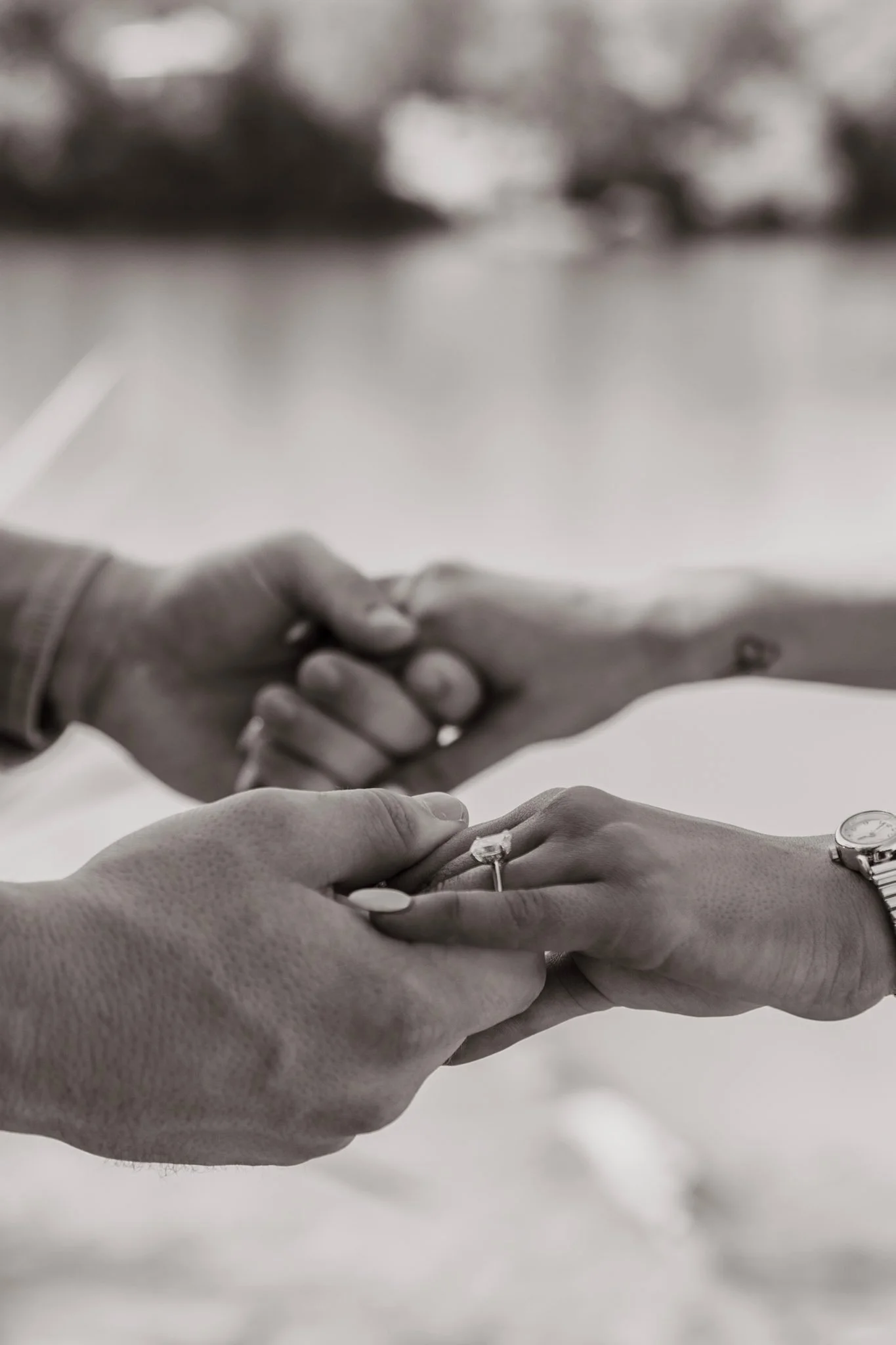 Two people holding hands during a wedding ceremony, one wearing a watch and a ring, the other wearing a ring and a bracelet, with a blurred background.