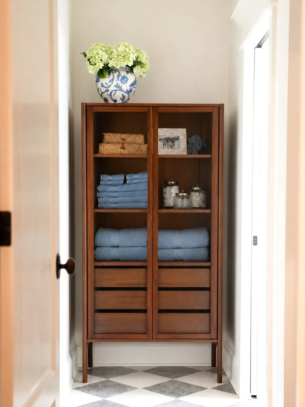 We reworked the layout of this bathroom, and took out the linen closet.

We added this walnut glass cabinet - storage that became a design moment. It just earned its place in the bathroom. Warm wood, folder blues,  a little collected coastal life on 
