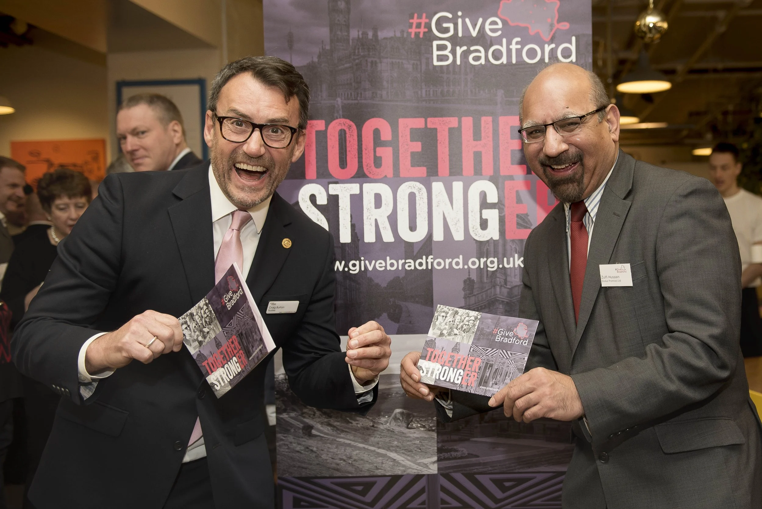 two businessmen in smart suits holding leaflets in front of a corporate banner. Event photographer Bradford