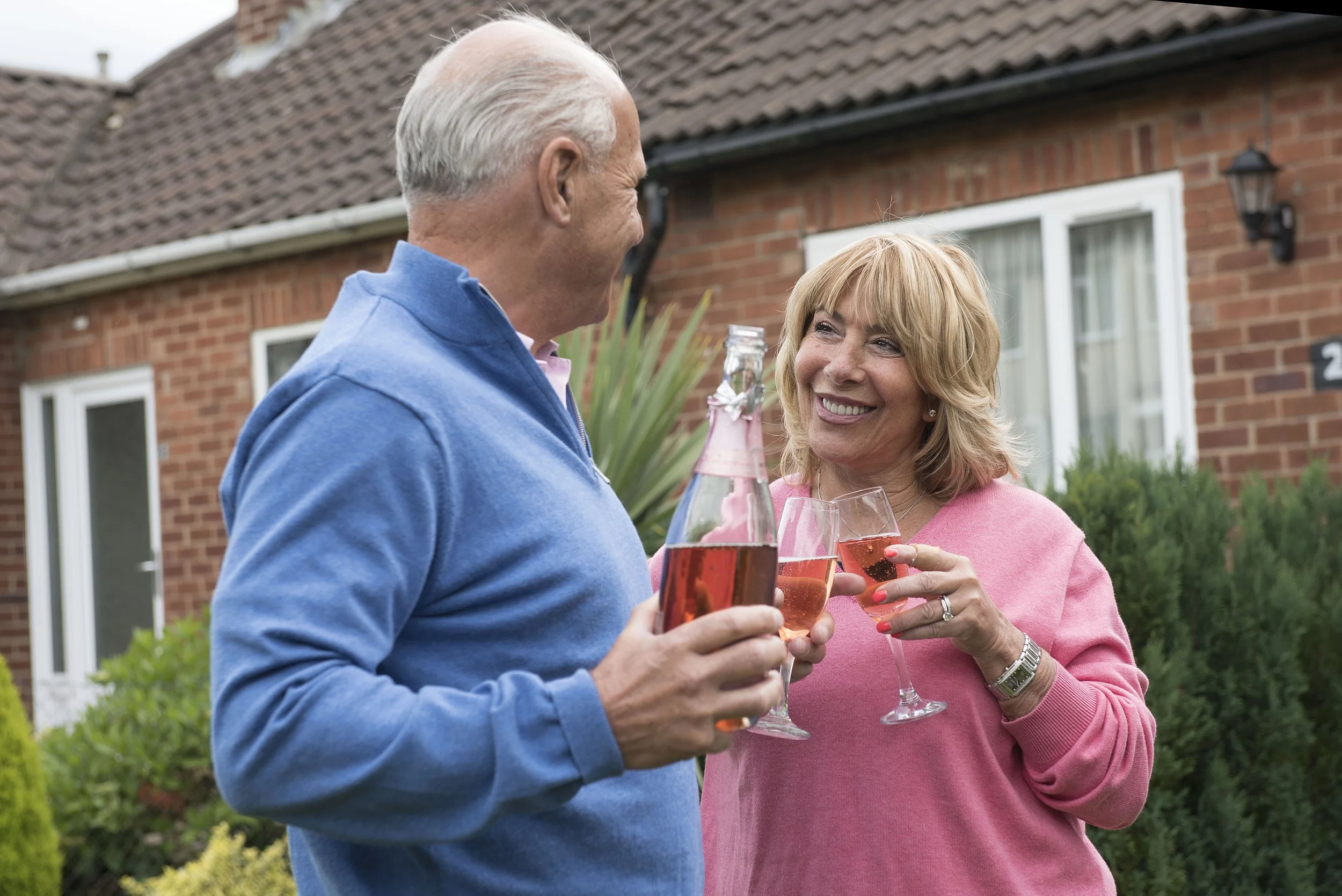 man and woman stood inside their from garden with a bottle of pink champagne and two glasses celebrating a like event