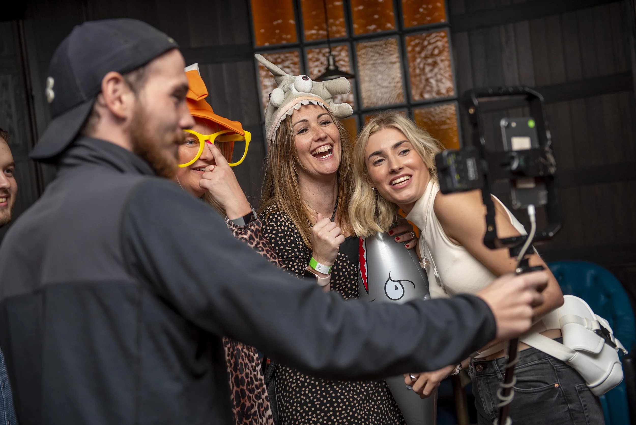 three women having a video taken at a party. wearing part hats and glasses. Event photographer Leeds