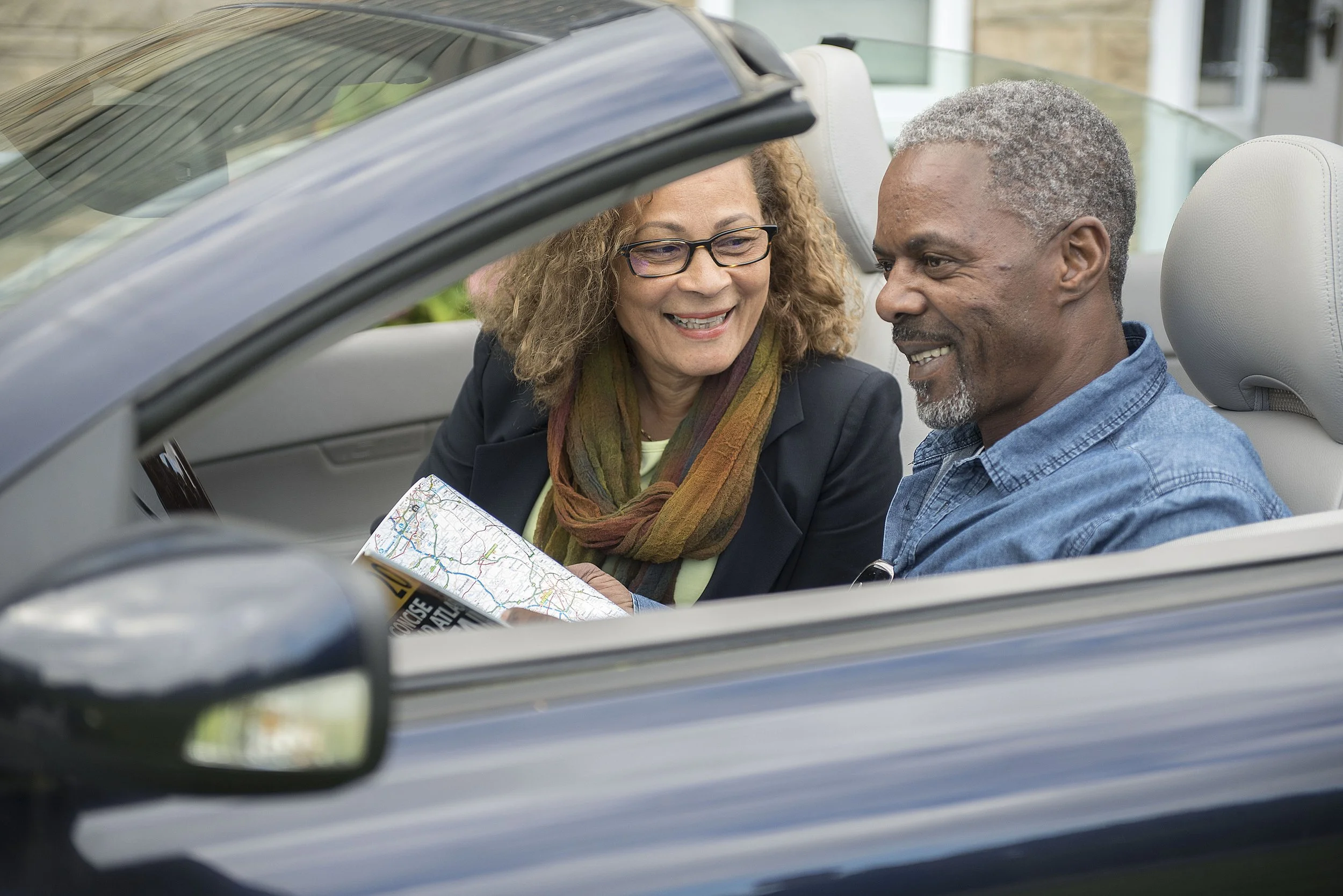a man and woman looking at a map whilst sat in the open top car 