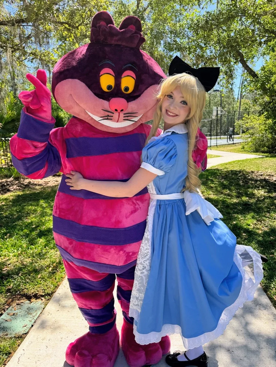 Alice in Wonderland hugging a large Cheshire Cat mascot at an outdoor Spring Egg Hunt and Easter Party in Tampa Bay