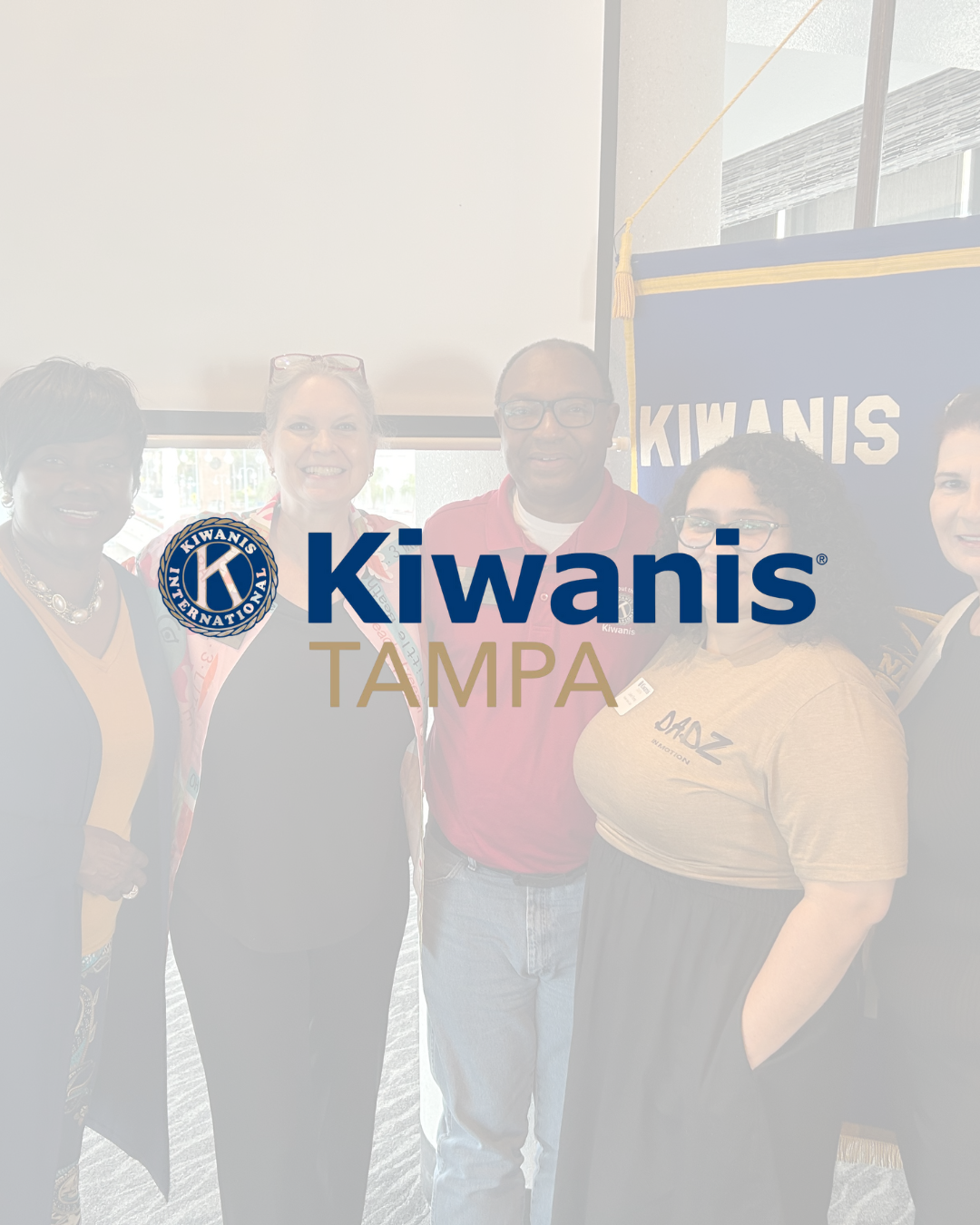 Group of five smiling people standing together at a Kiwanis event, with a Kiwanis banner in the background.