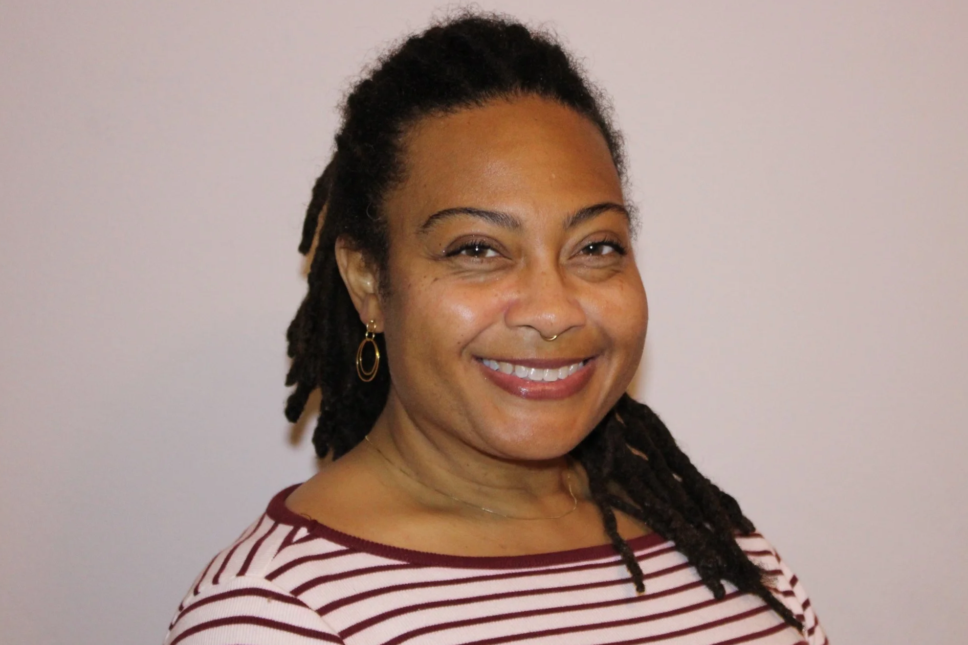 Smile of a woman with dark hair styled in dreadlocks, wearing a striped shirt and gold hoop earrings.