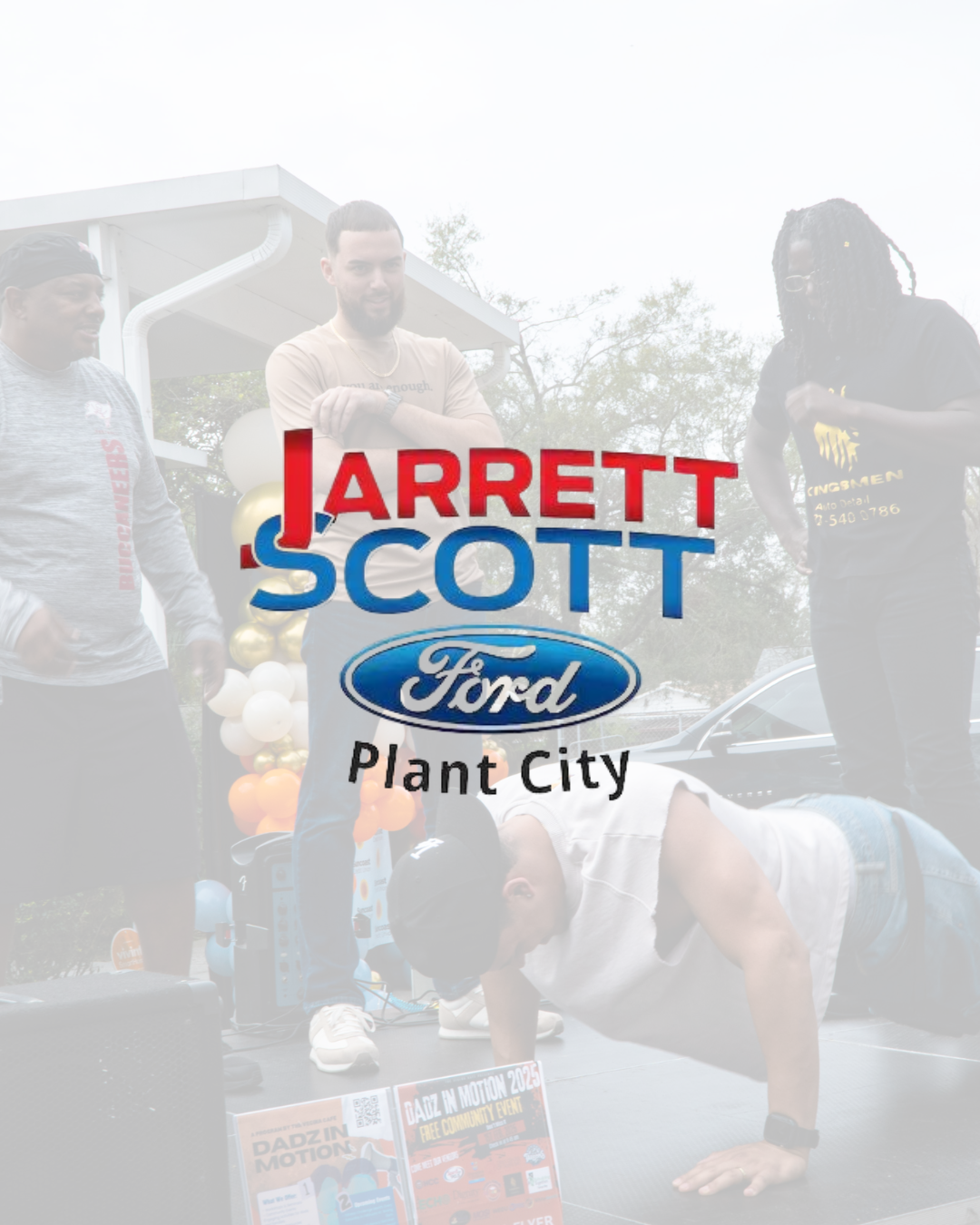 Group of people participating in a community event outdoors, with some standing and one person performing a push-up on a stage, promotional materials and balloons in the background, and a logo overlay for Jarrett Scott Ford Plant City.