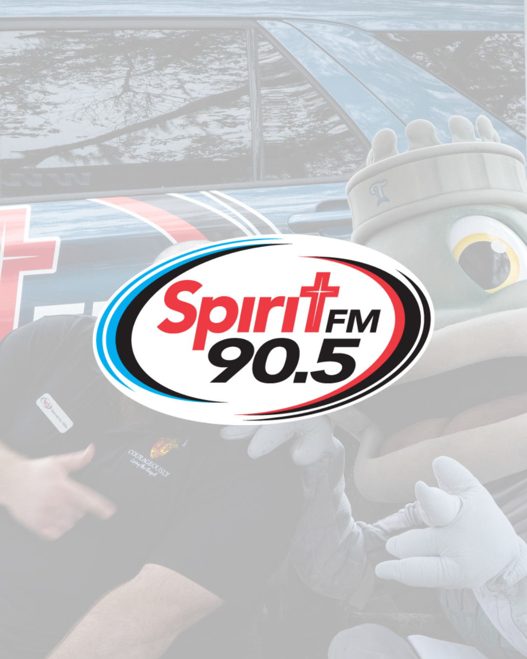 Radio station logo 'Spirit FM 90.5' on a racing car with a mascot and team members in the background.