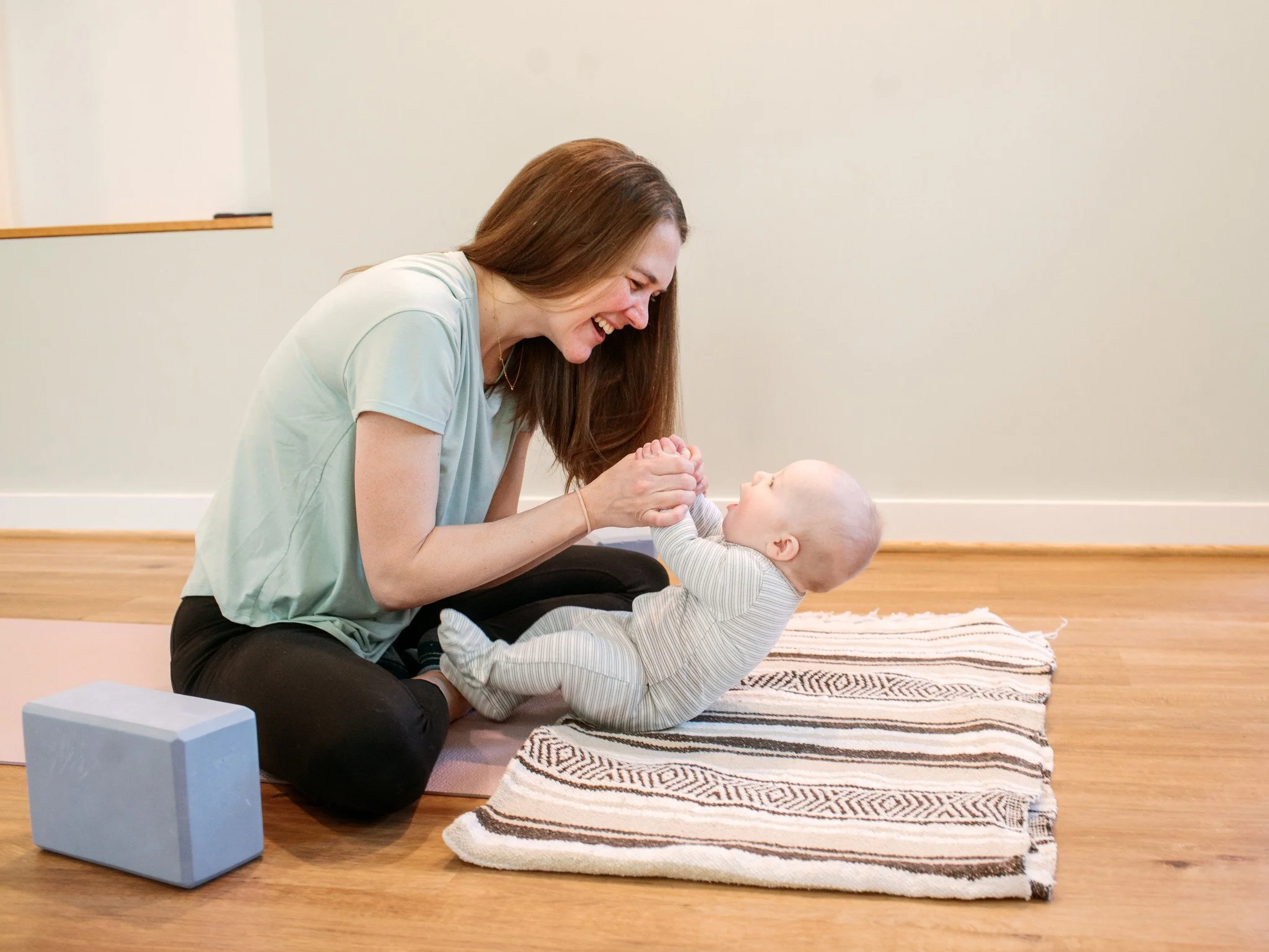 A white woman holding the hands of their baby, pulling them into a sitting position on the floor