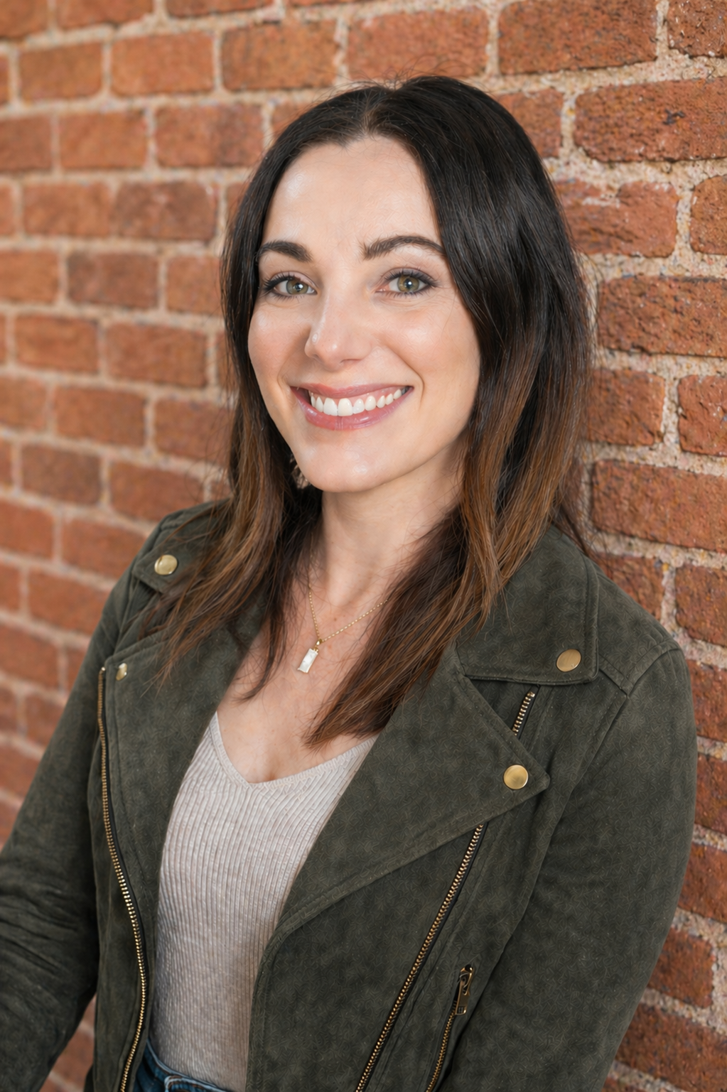 white woman with brown hair leaning against a brick wall and smiling
