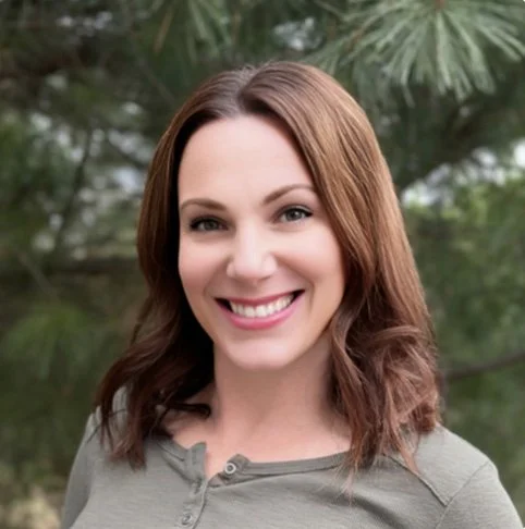 Picture of Lynn, a white woman with brown hair in a green buttoned shirt in front of an evergreen tree