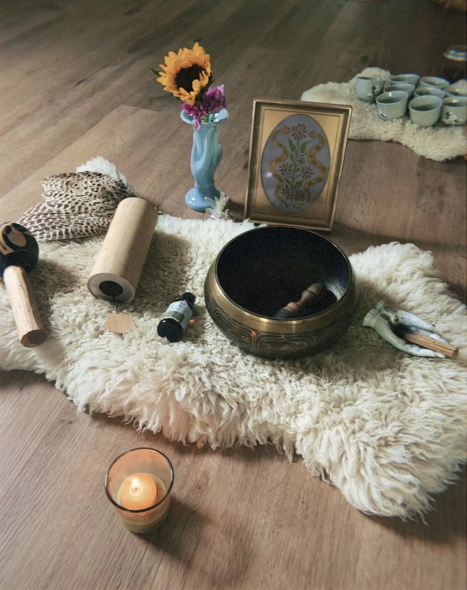 a fake fur rug with Tibetan singing bowl, chime, feather and gong along with a lit candle and flower