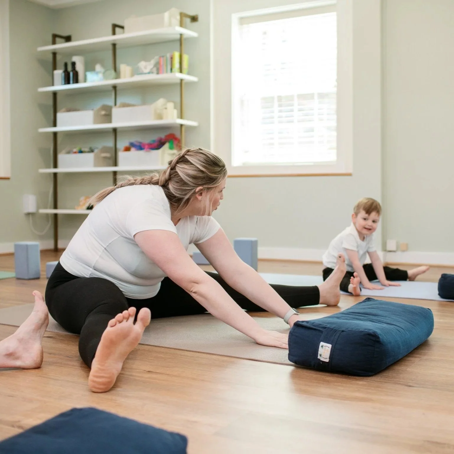 A woman is doing a yoga pose and kissing a small child in a red sweater