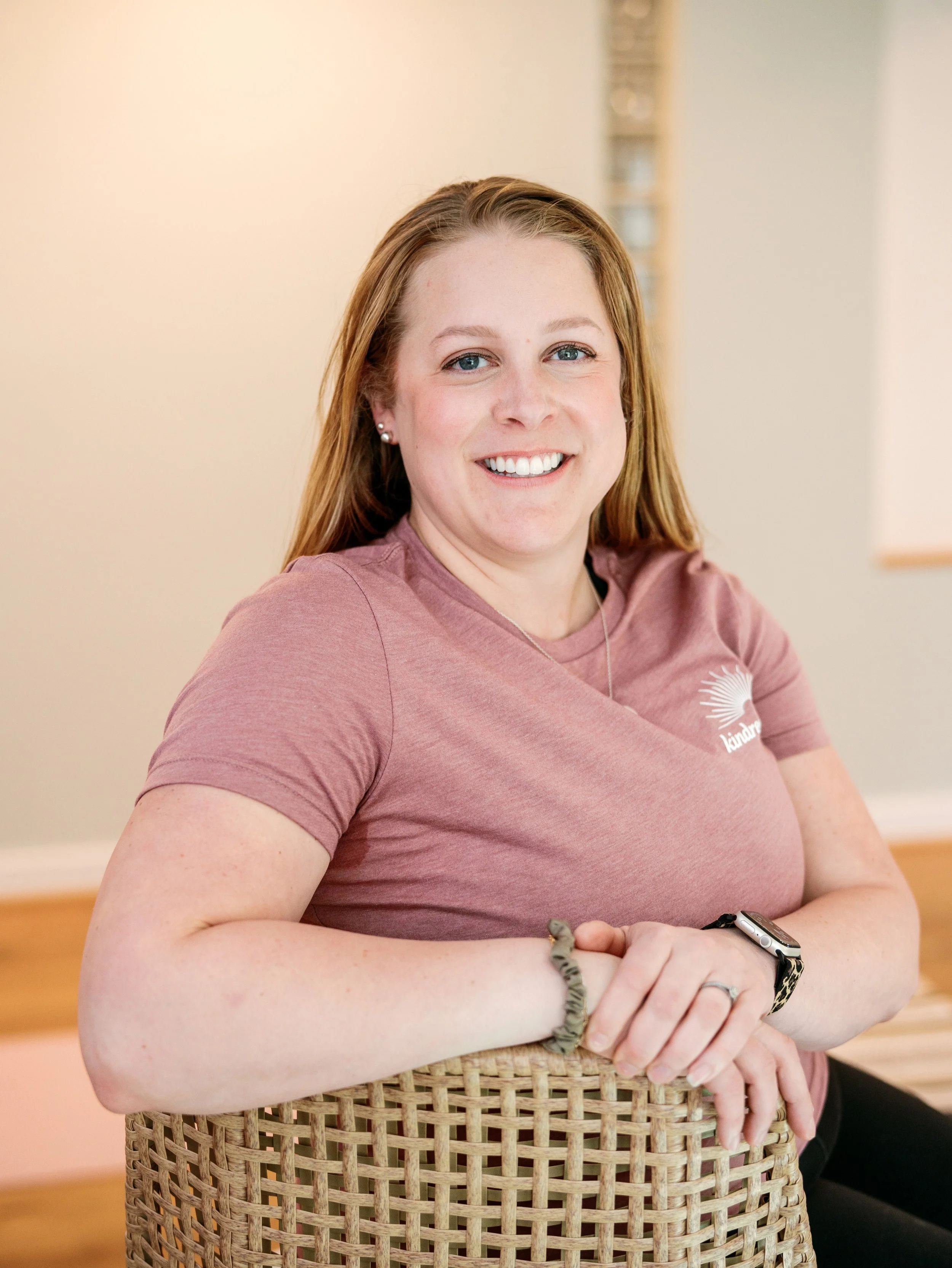 white woman with straight hair sitting on a stool with her arm over the back smiling
