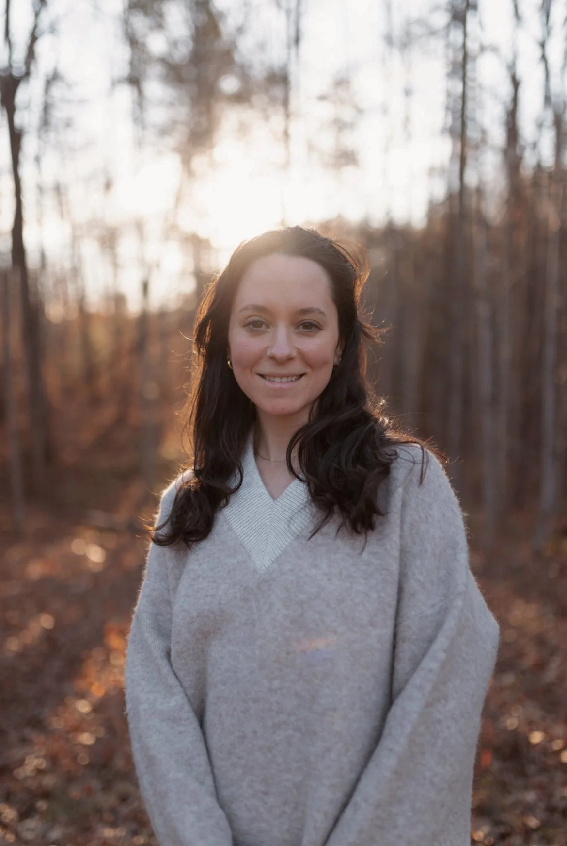 Elena, a white woman with brown hair standing in a field with trees behind her