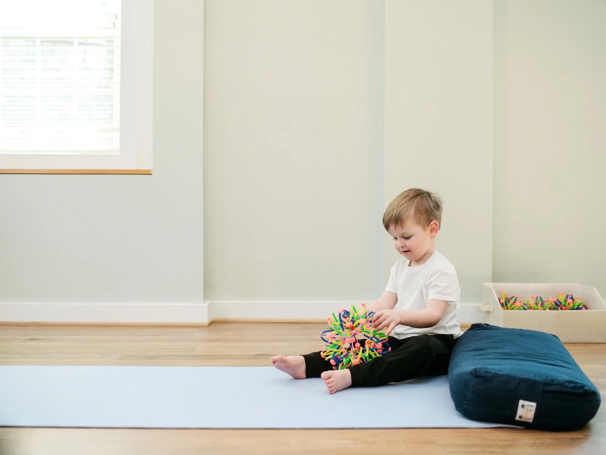 a young boy sitting on a yoga mat with a breath ball