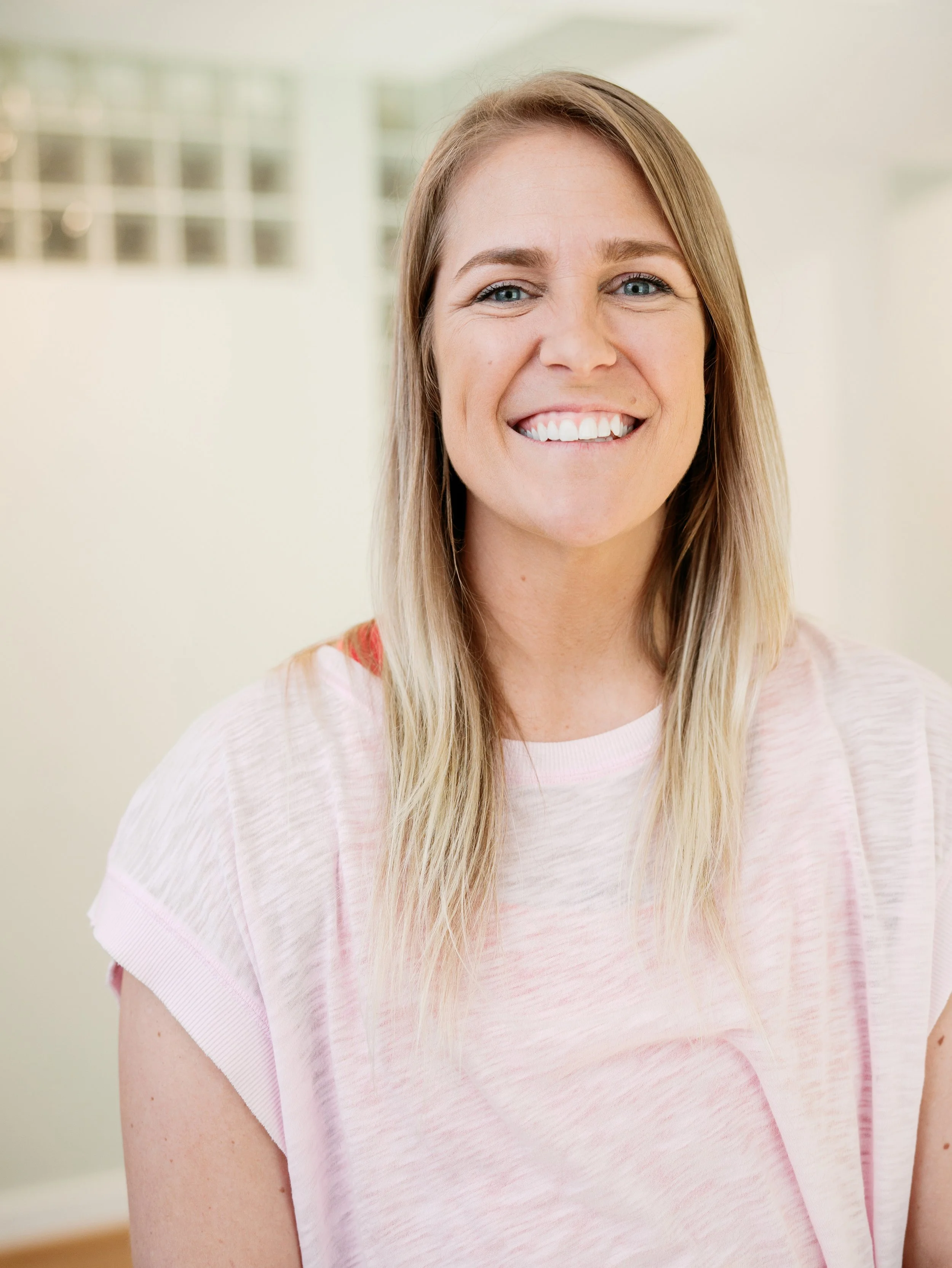 A white woman smiling in a pink shirt with blonde hair 